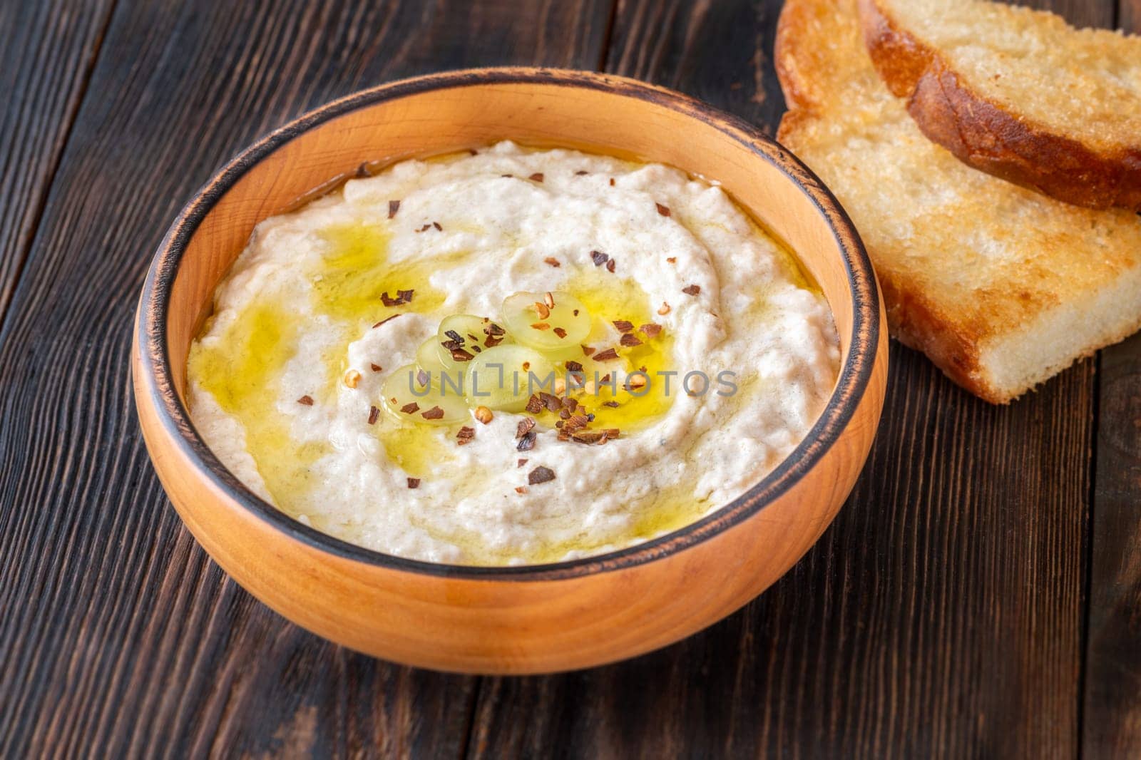 Roasted eggplant dip topped with chili flakes and oil in rustic setting