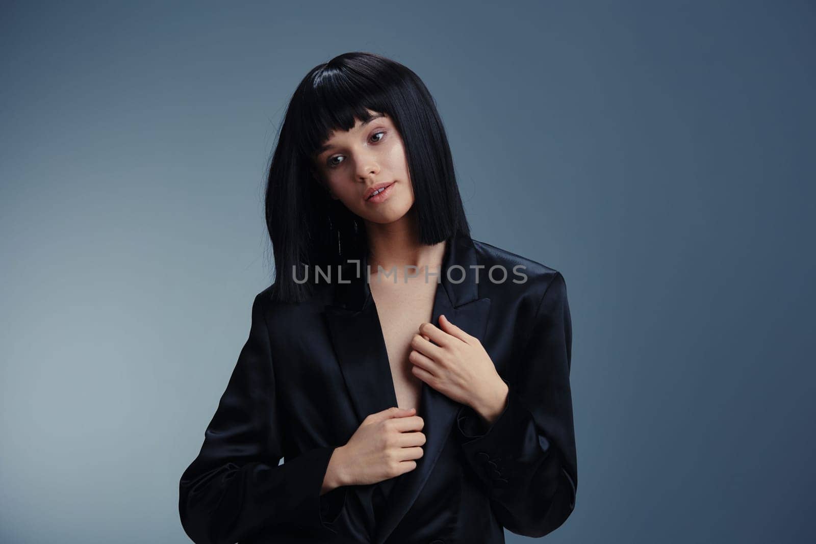 Black suit woman posing with hands on hips, looking off to the side, exuding confidence and professionalism in a studio setting