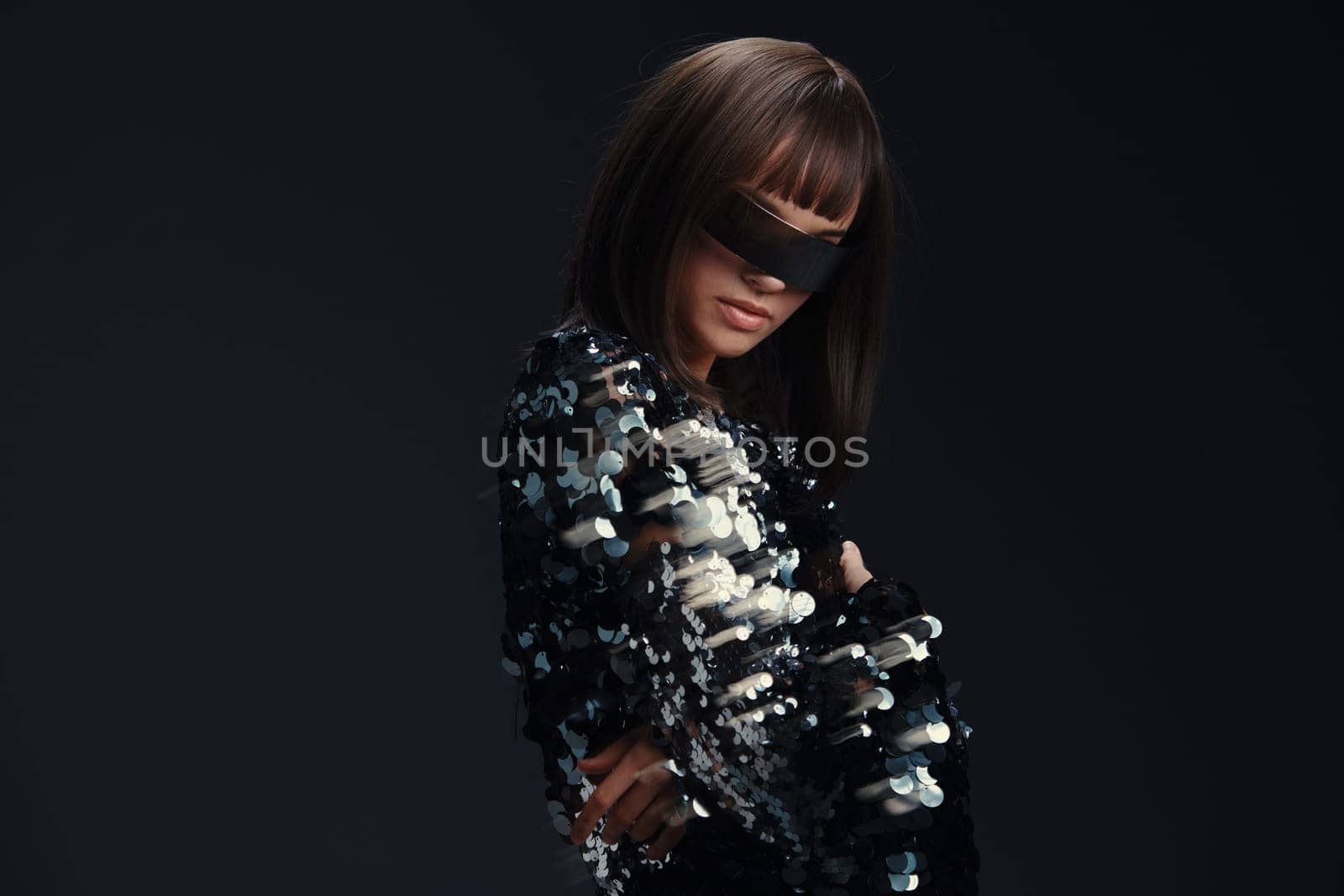 Woman in black and white dress, blindfolded, wearing necklace and head scarf, posing against neutral background, evoking themes of mystery, fashion, and intrigue