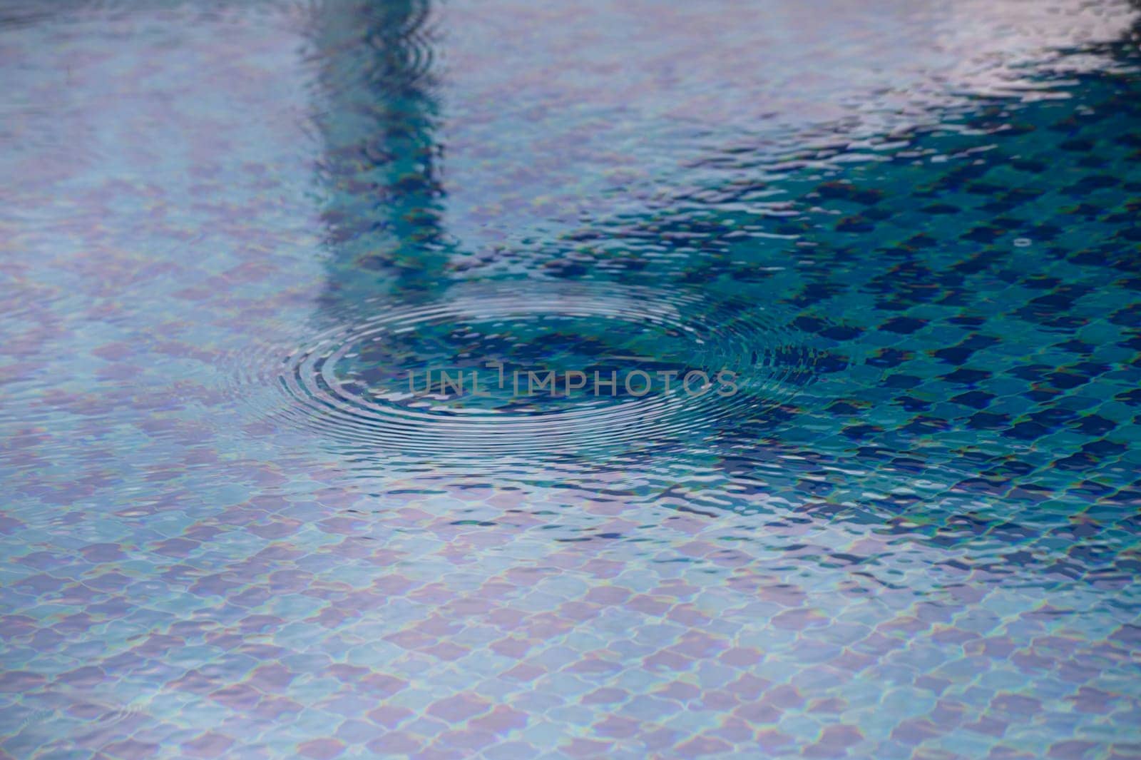 In the heart of a sunlit afternoon, gentle ripples form on the calm surface of a vibrant blue pool. The clear water reflects the surrounding beauty, inviting tranquility and relaxation.