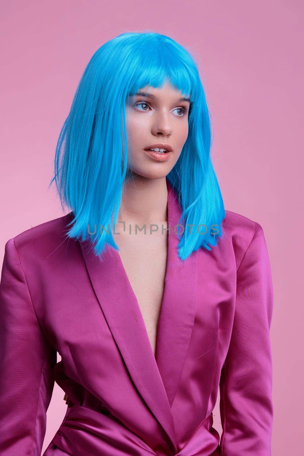 Woman with bright blue wig wearing pink suit, standing against pink background, exuding vibrant and playful energy, perfect for themes of fashion, individuality, and bold color contrast