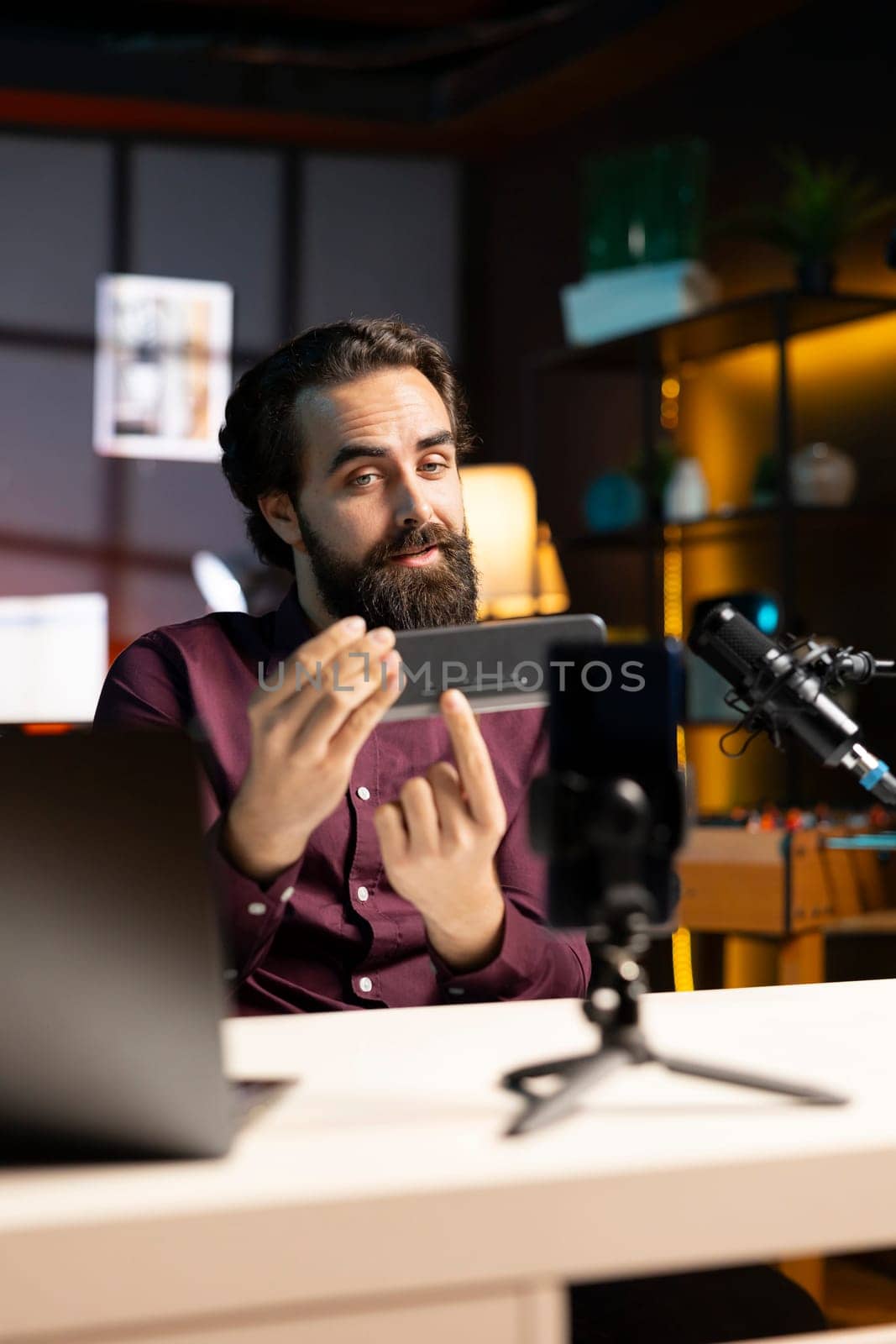 Tech guru informing audience about newly released mini soundbar. Man in studio pressing buttons on high end music playing device, testing specifications, filming with smartphone