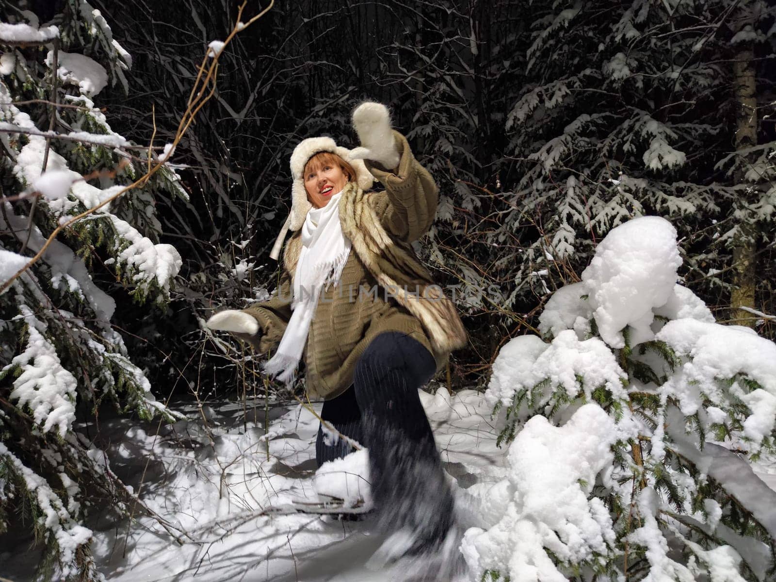 A middle-aged woman dressed warmly walks playfully through the snow-covered woods at night, showcasing her humorous side with a balalaika.