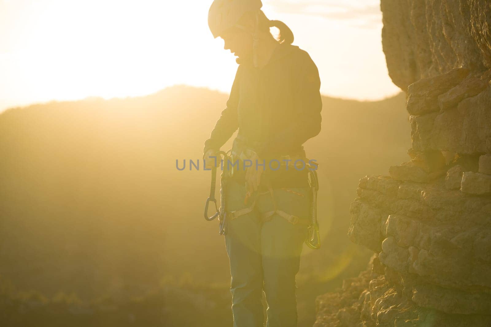 Young girl is preparing for training on the rocks sunset, in the mountains and puts a helmet on her head for safety to protect her health, woman engaged in active sports, in mountaineering and rock climbing.