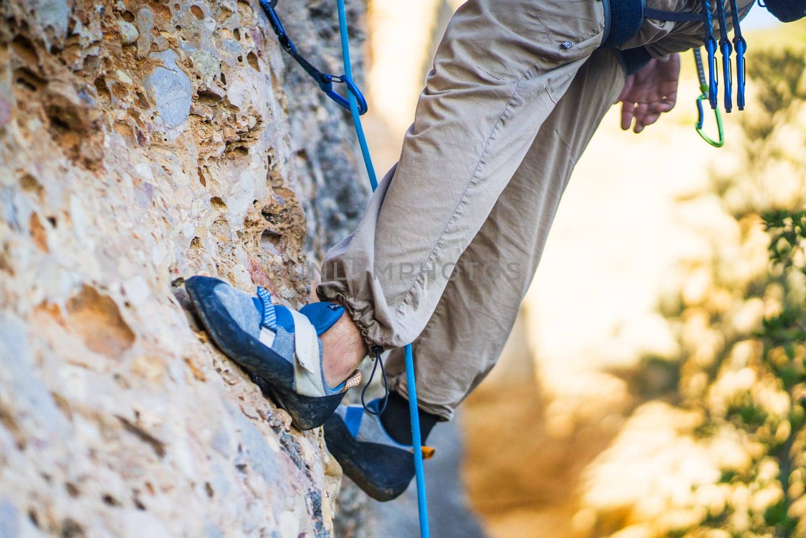 A person climbs the mountain in special climbing shoes, close-up view of the legs with copy space. A woman is engaged in active extreme sports, mountaineering and climbing.