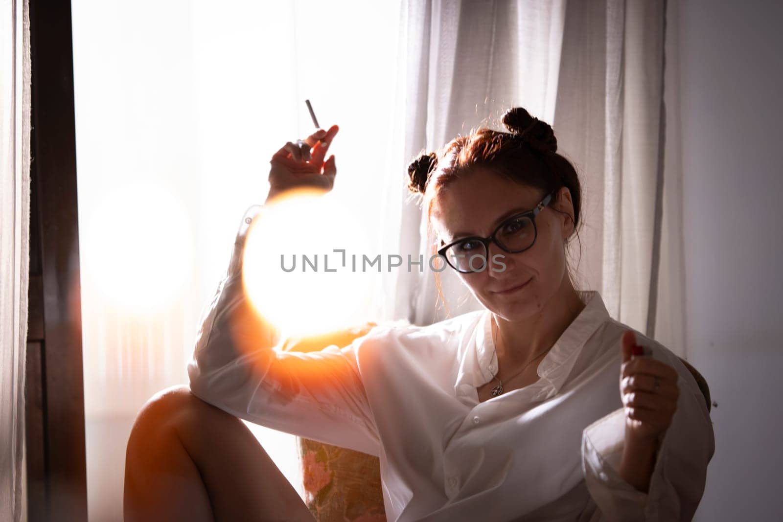 Relaxed woman smoking a cigarette sitting by the window in natural sunlight