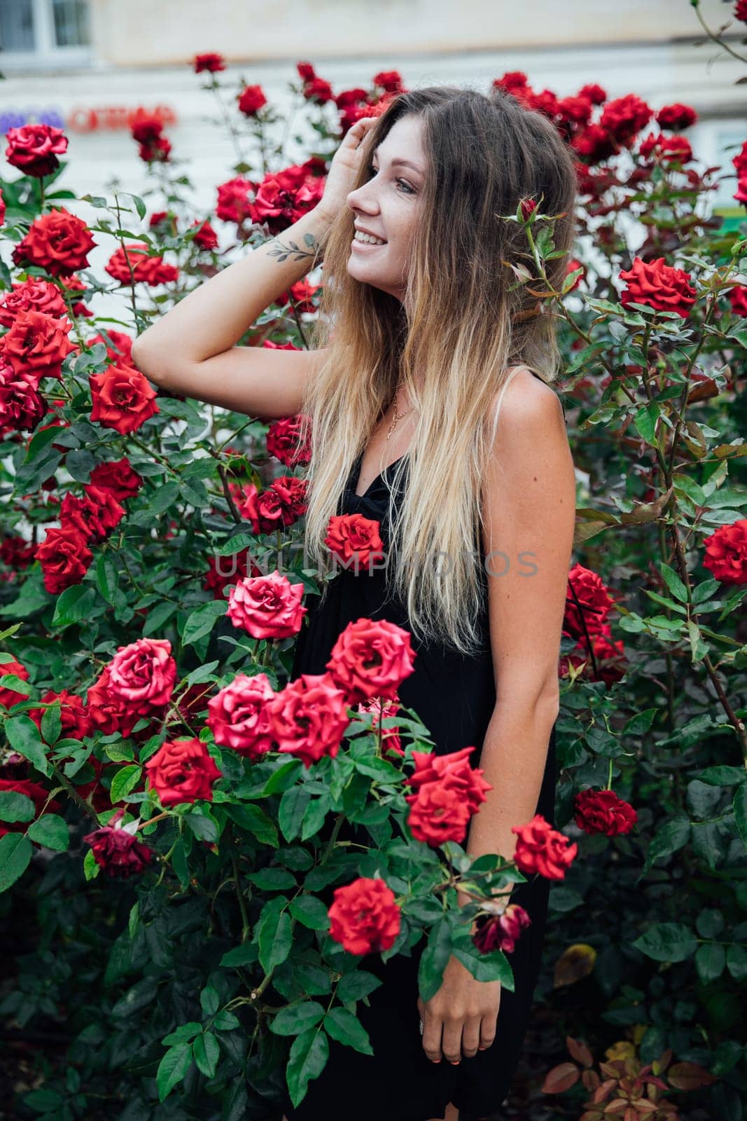 Beautiful woman in black summer dress smiling among red rose flowers