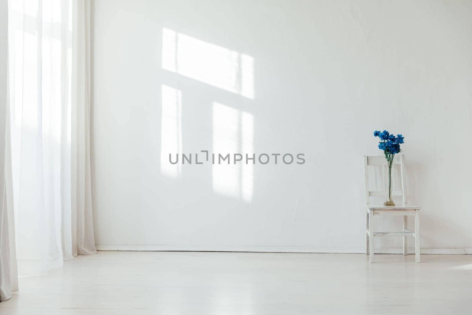 One vintage chair and vase with blue flowers in the interior of a white room with a window