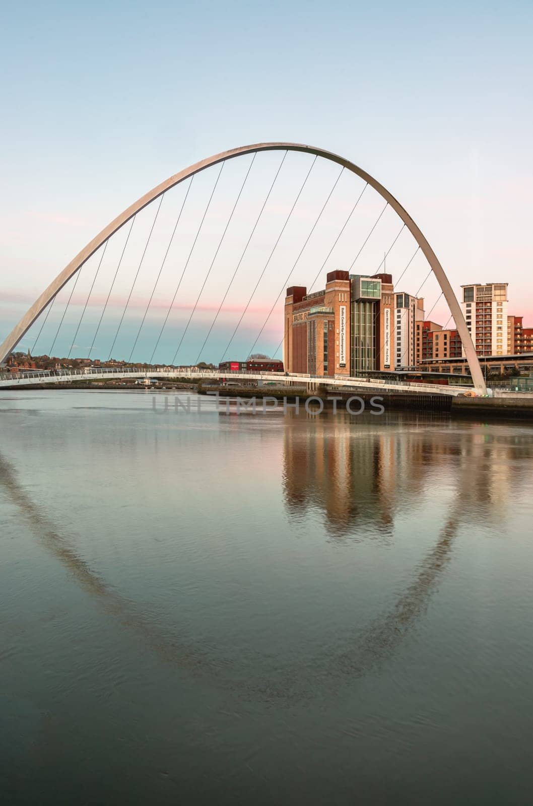 Newcastle, UK - Apr 13, 2025 - Beautiful scenery of The Iconic Gateshead millennium bridge spanning the River Tyne and Baltic flour mills with Magnificent sky in the background after sunset. The pedestrian bridge with reflection in the river, use it as your Wallpaper, Poster and Copy space, Selective focus.