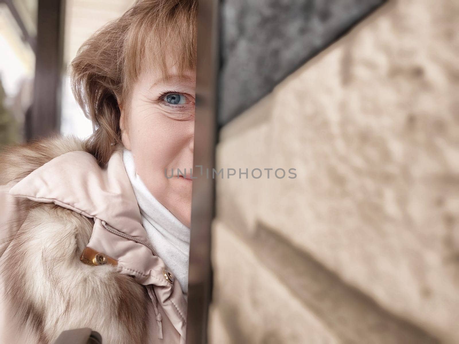 Middle-aged woman takes a playful selfie while peeking from behind a wall, capturing a lively moment during her travel adventure.