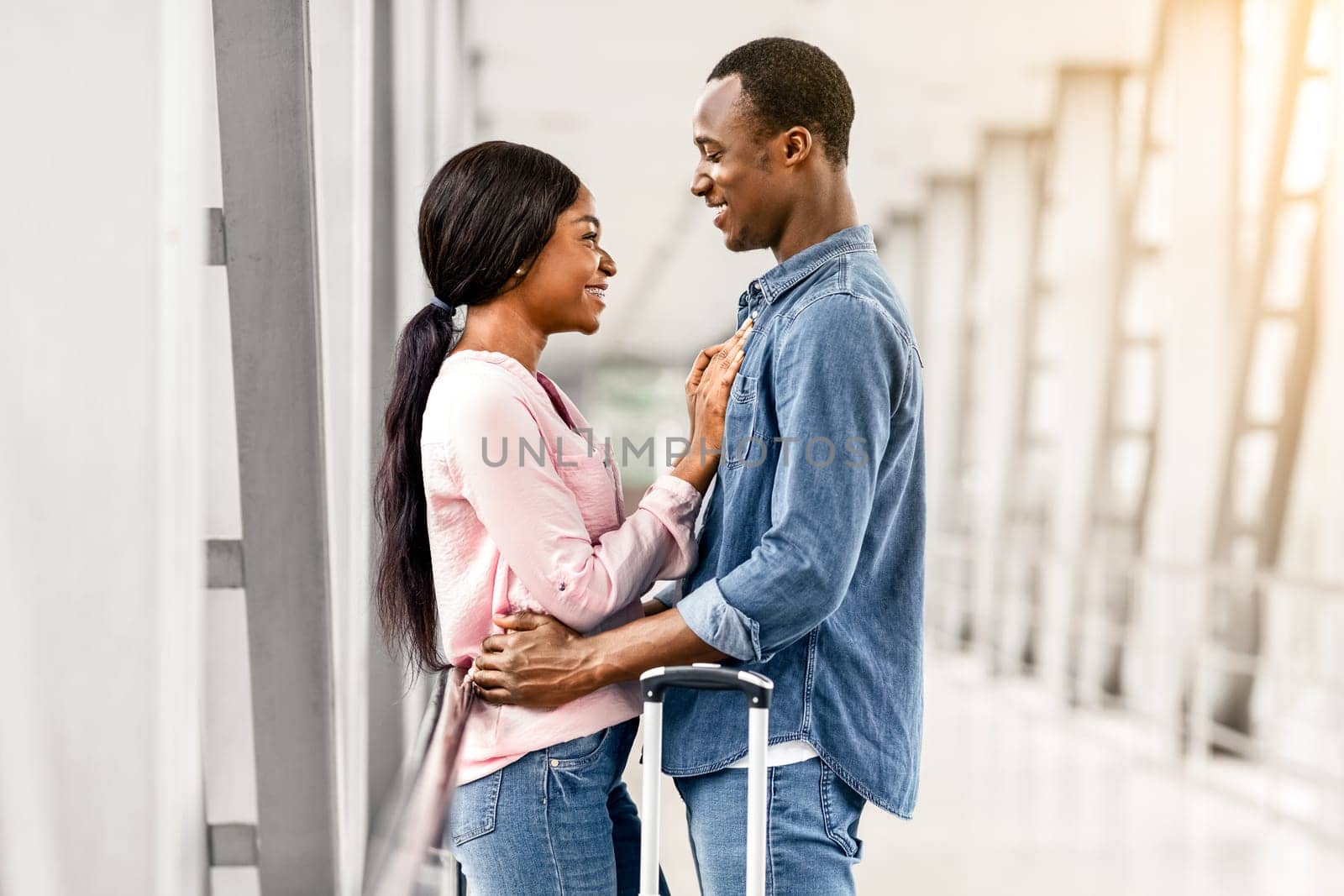 Loving African American Man And Woman Cuddling In Airport Terminal Before Flight, Happy Romantic Black Couple Waiting For Plane Boarding, Ready For Honeymoon Vacation Trip, Side View With Free Space