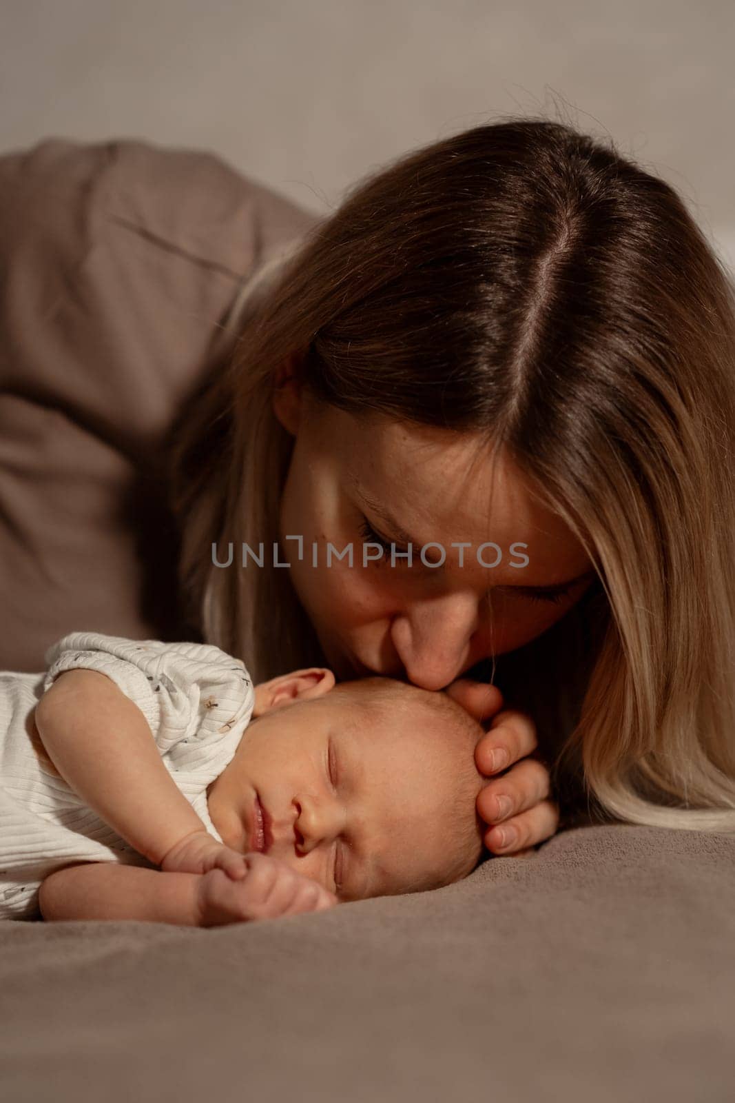 Mother gently kisses her sleeping baby, creating a serene and intimate moment in their cozy home environment, highlighting their bond and affection.