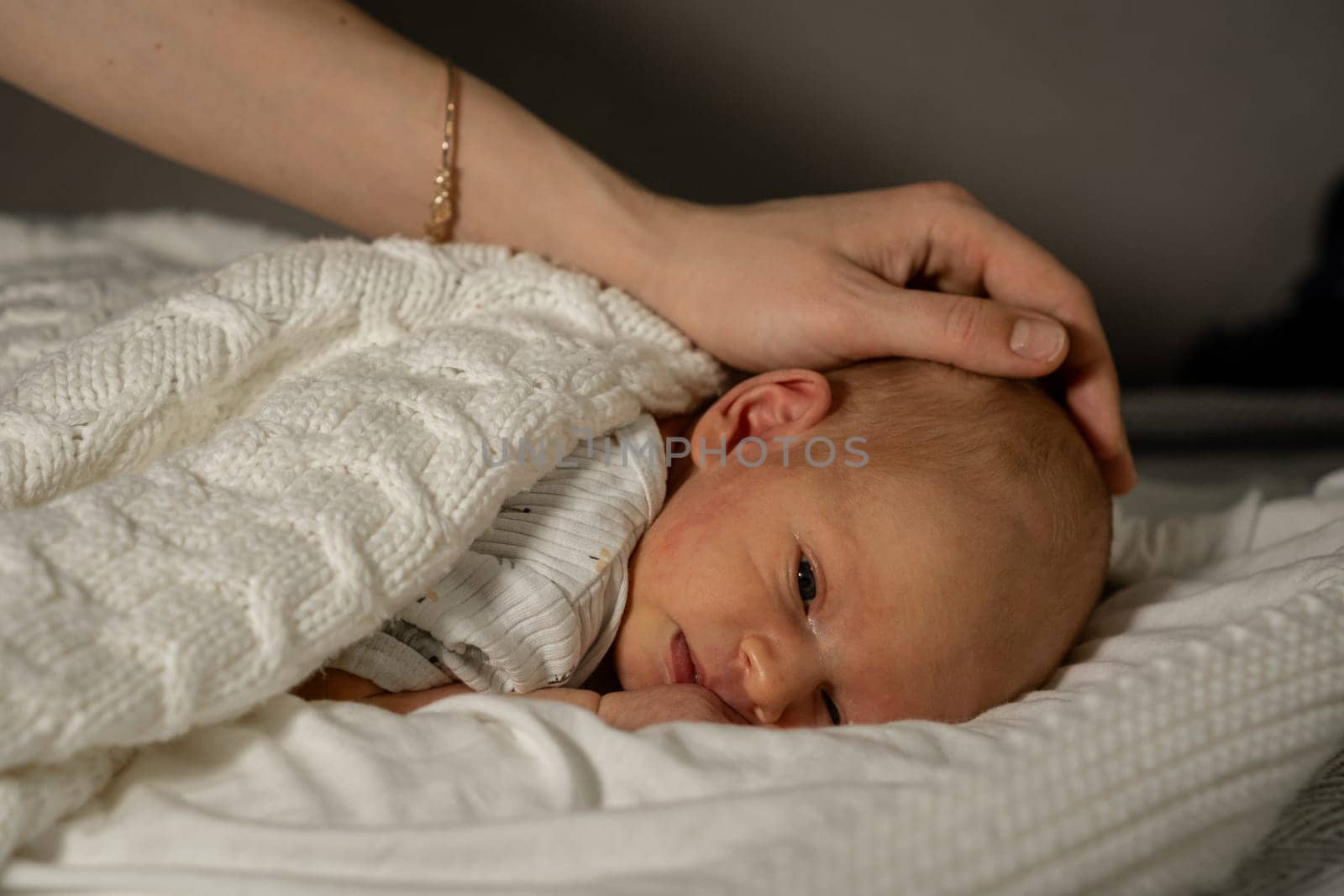 A mother gently caresses her sleeping newborn, wrapped warmly in a soft blanket in a serene and cozy environment during the evening.