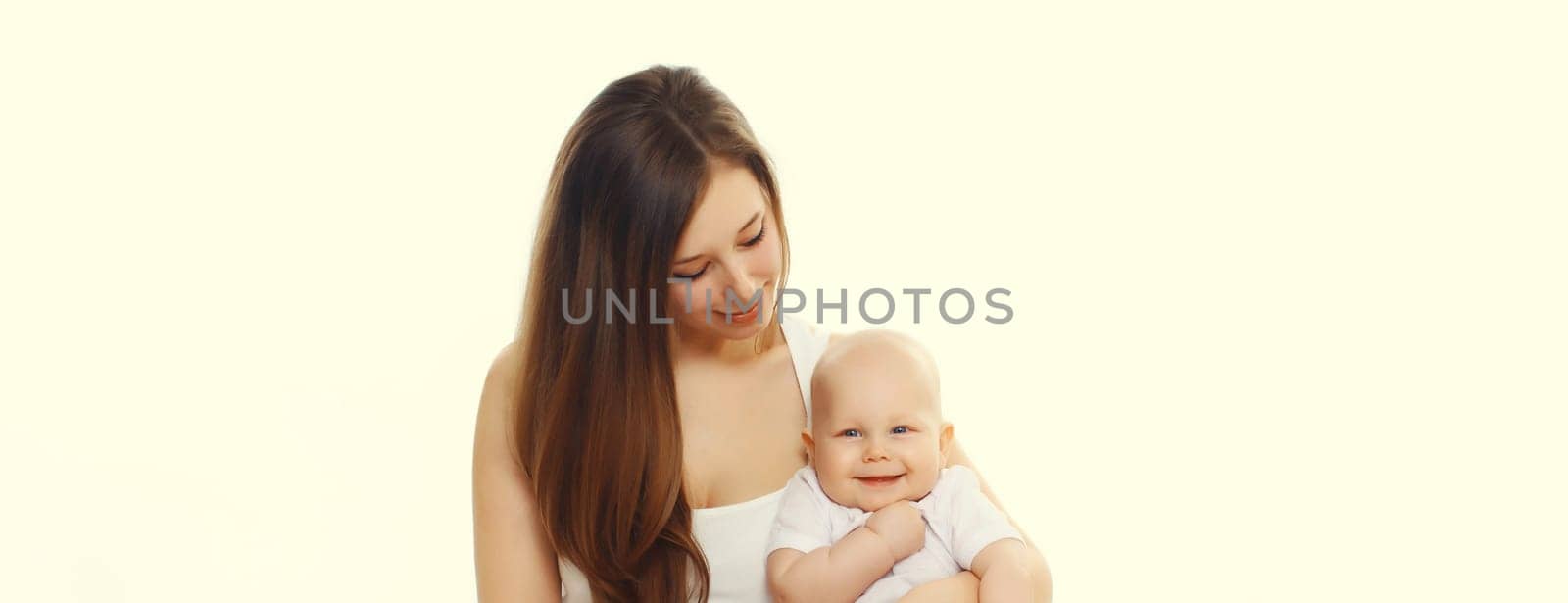 Happy smiling young mother playing with cute baby sitting together on the floor on white studio background