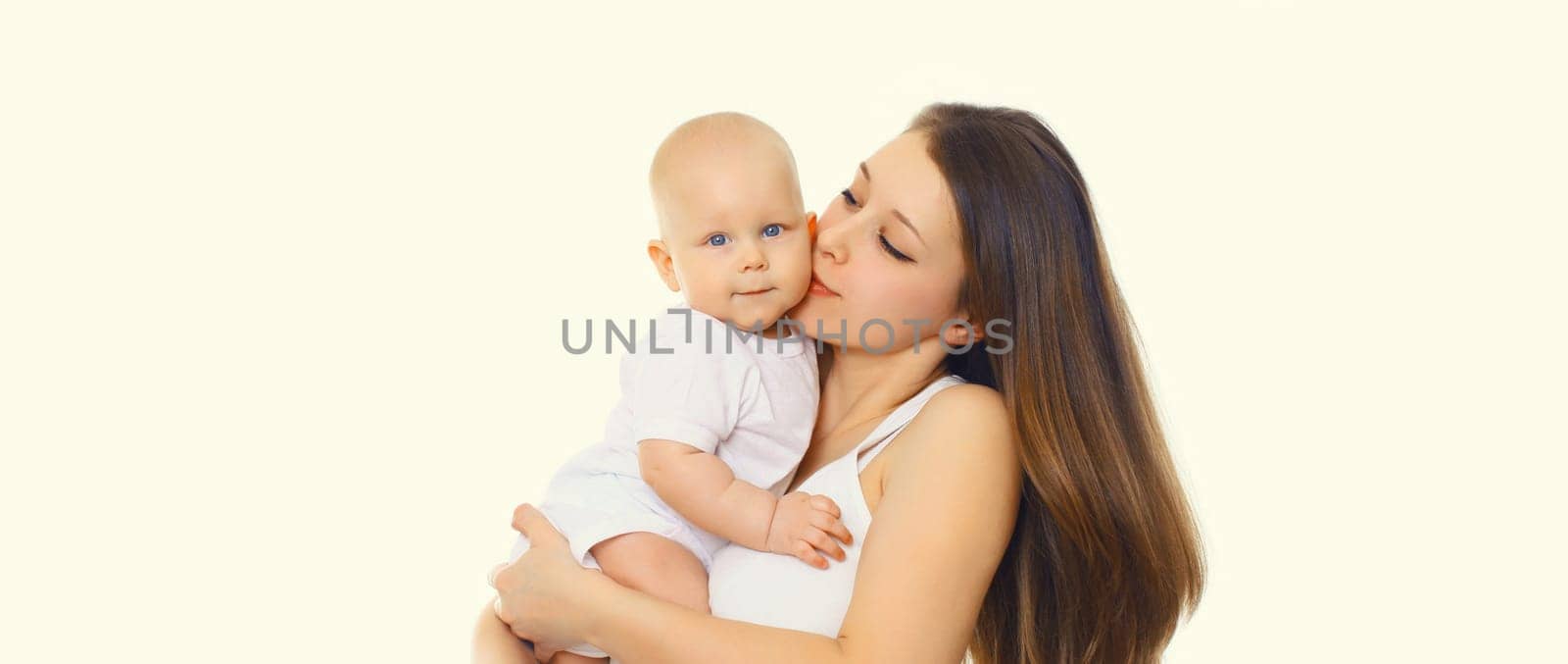 Portrait of happy mother kissing holding her baby, young mom and little child on white studio background