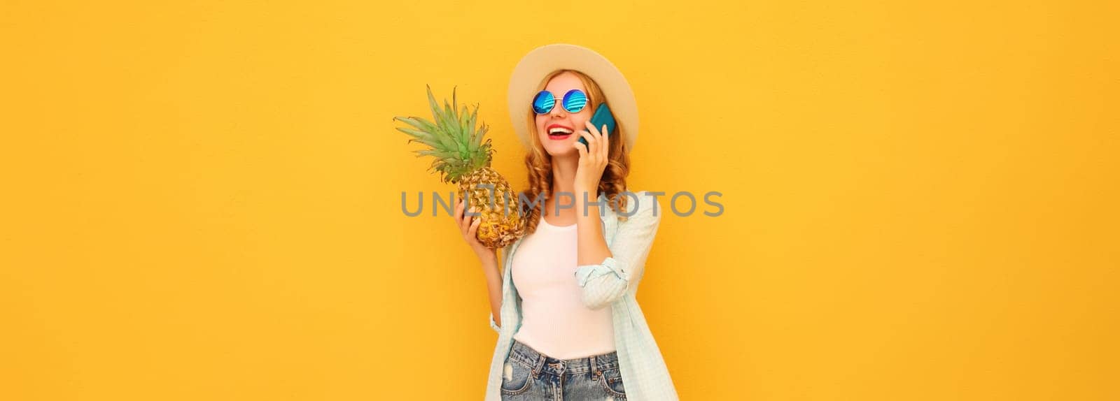 Summer vacation, happy joyful woman calling on phone with pineapple fruit in tourist hat, cheerful girl talking on the smartphone on yellow studio background