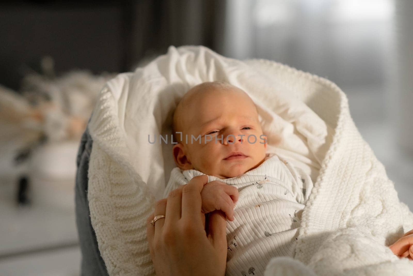 A mother cradles her infant in her arms while they sit together in a serene indoor setting. The soft sunlight creates a warm atmosphere.