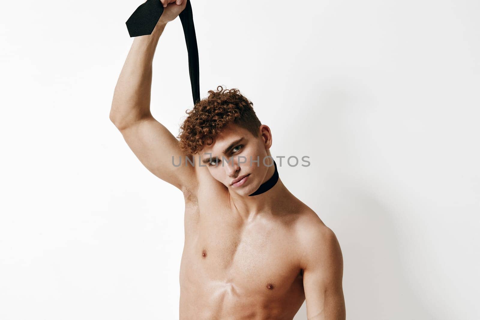 A striking, shirtless male model confidently poses with a black tie in an elegant, modern, minimalistic setting