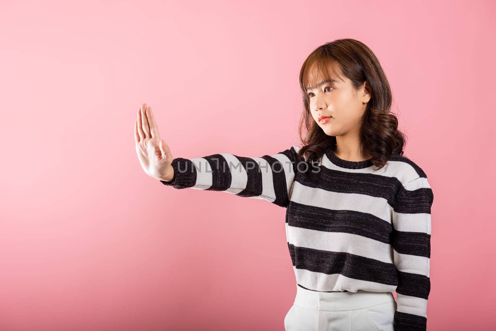 Asian portrait beautiful cute young woman teen smiling doing show stop sign gesture with palm of hand but happy face studio shot isolated on pink background, female doubt with copy space