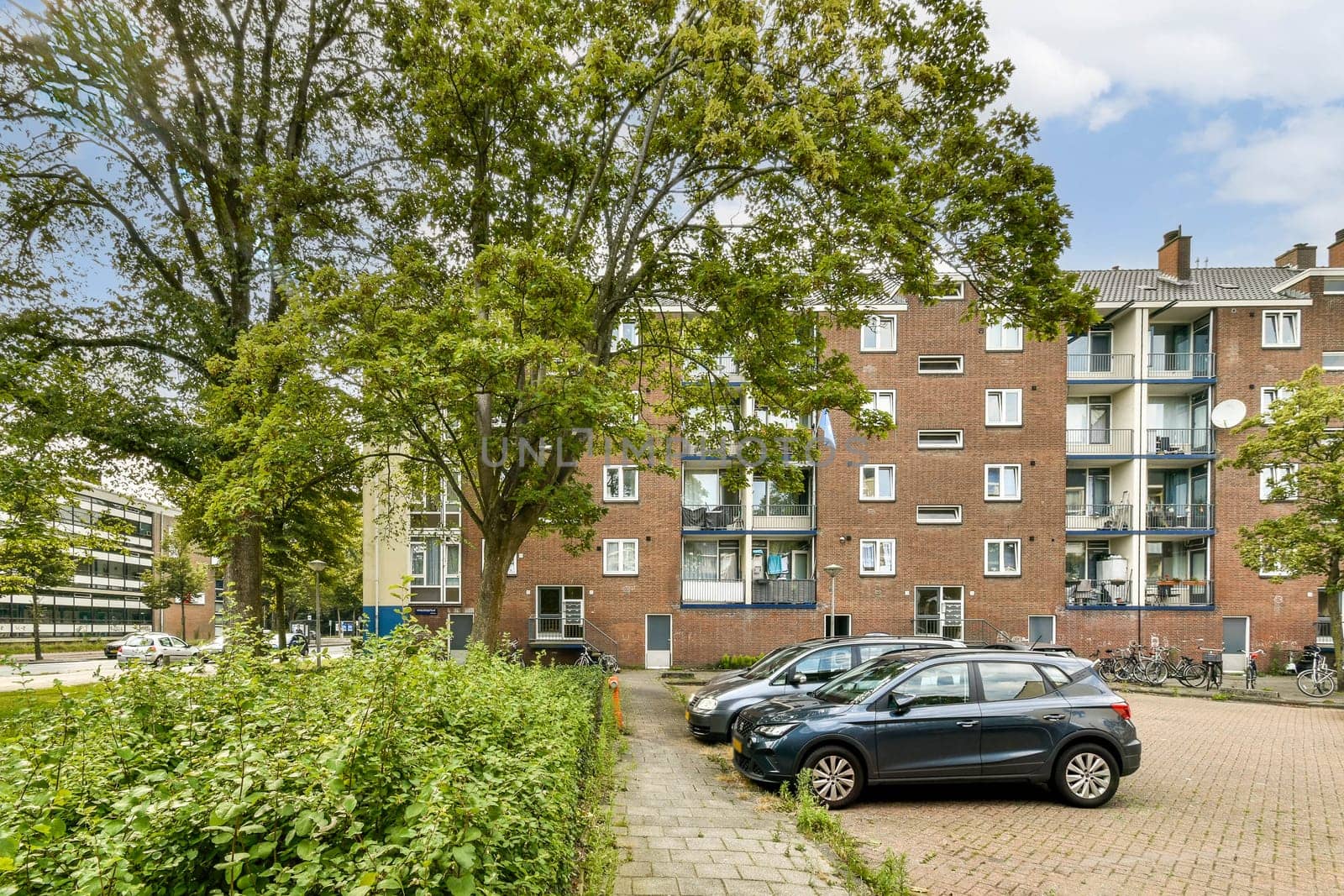 A contemporary apartment complex surrounded by lush greenery and parked cars, showcasing urban living in harmony with nature.