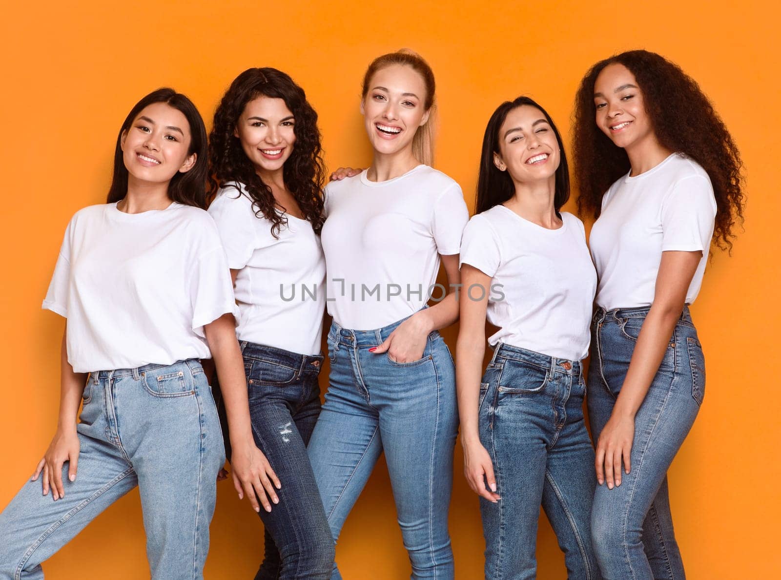 Five Happy Young Women Of Diverse Ethnicity Posing Together Smiling Looking At Camera Standing On Yellow Background In Studio, Wearing White T-Shirts. Diverse Friendship And Multiracial Female Beauty