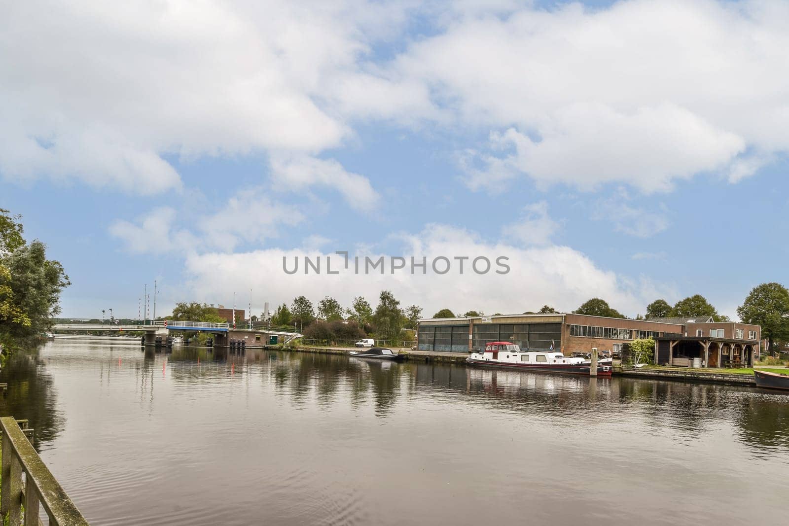 A picturesque waterside scene showcasing boats moored along a serene riverbank, surrounded by lush greenery and beautiful cloud formations.