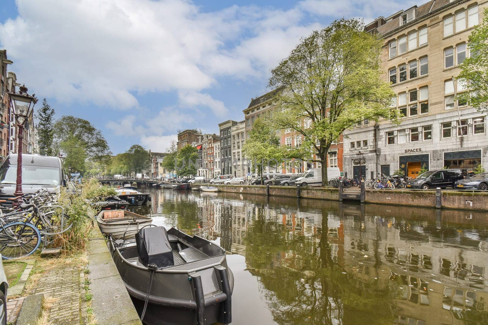 A picturesque view of a canal in Amsterdam surrounded by lush trees, lined with bicycles, showcasing the vibrant city life and architectural beauty.