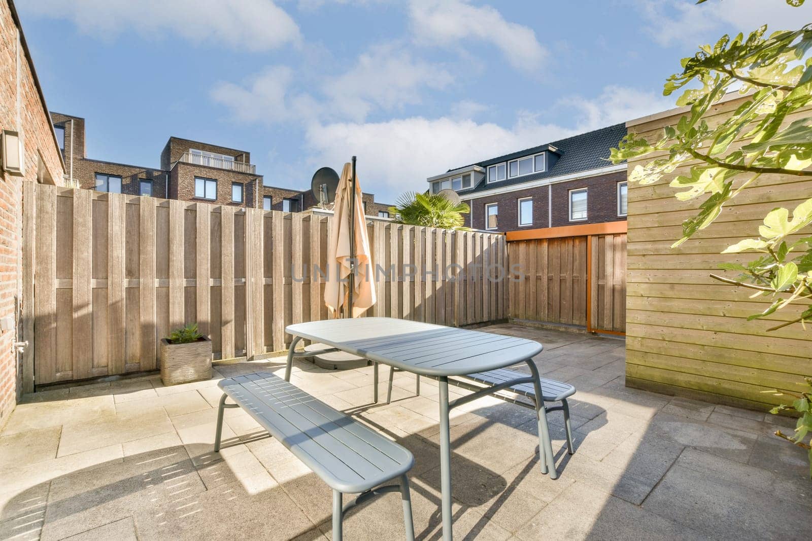 A bright and inviting outdoor patio featuring a table and bench set against a wooden fence, perfect for relaxation and dining in the sun.