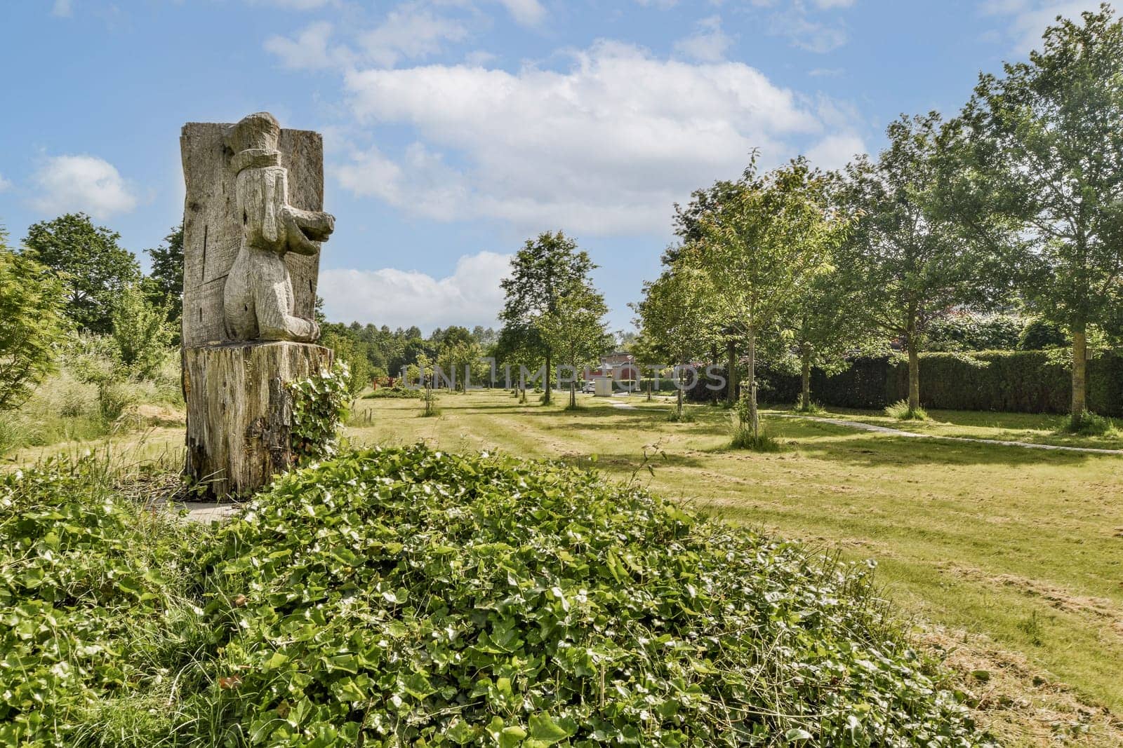 A striking wooden statue stands prominently amidst a verdant landscape, surrounded by trees and manicured grass, showcasing natural beauty and artistry.
