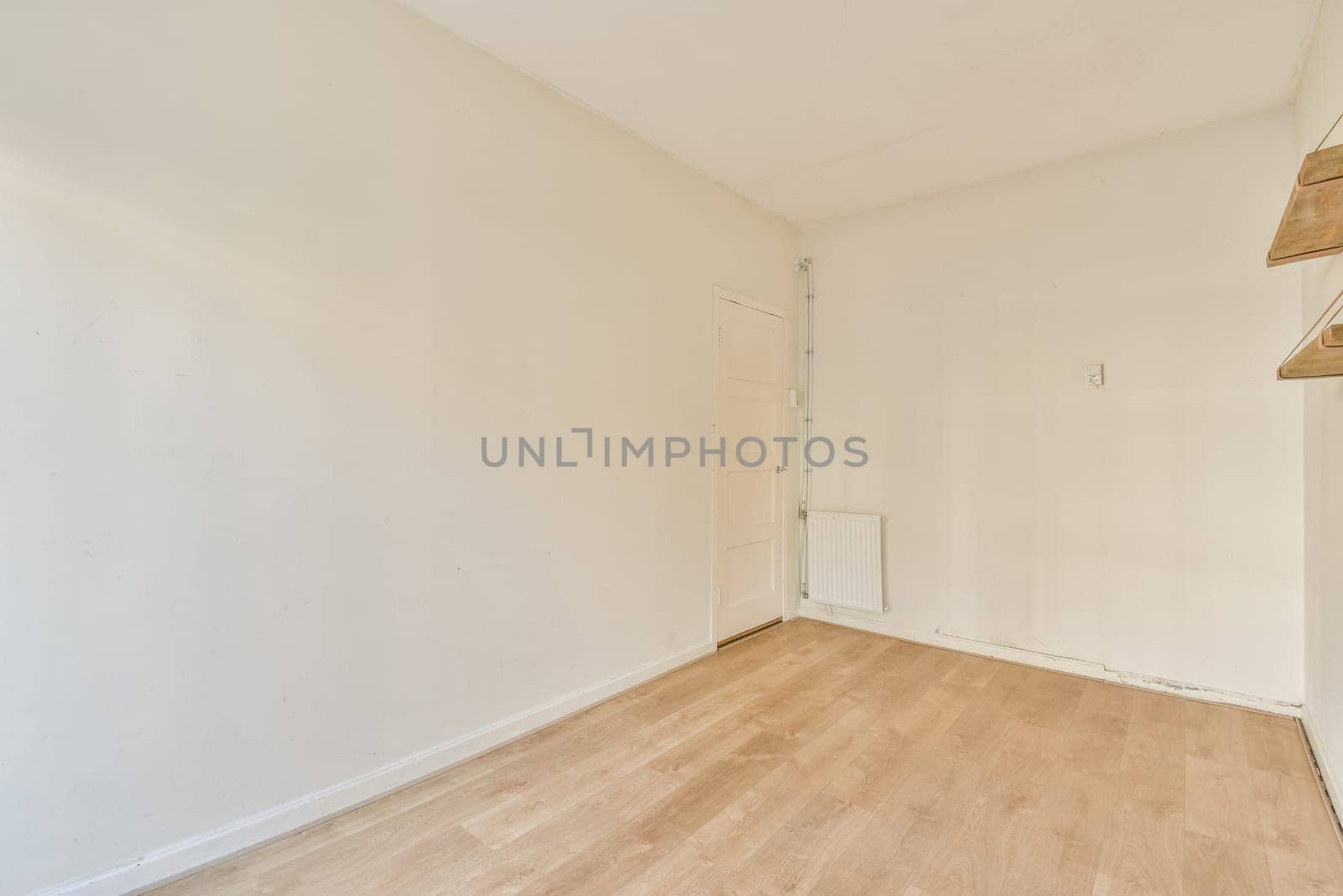 A spacious, minimalist room featuring light-colored walls and a simple wooden floor. The absence of furniture gives it a clean and airy ambiance.