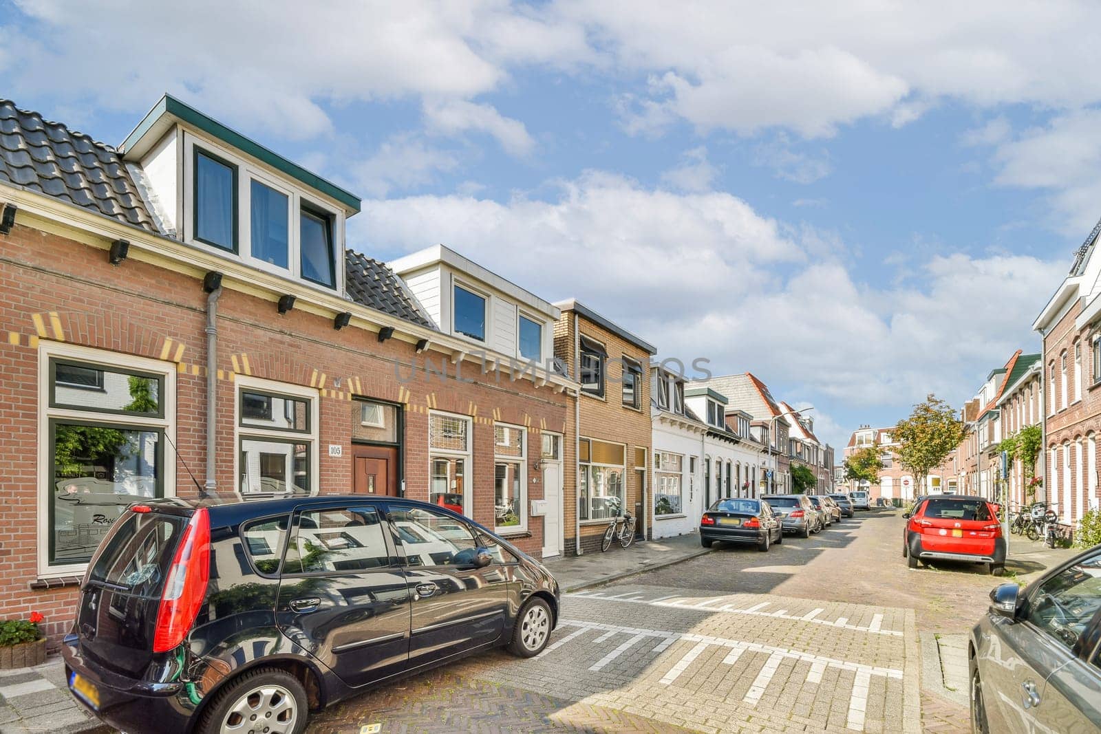 A picturesque view of a quiet urban street lined with cozy buildings and parked cars, set against a clear blue sky. Perfect for showcasing city life.