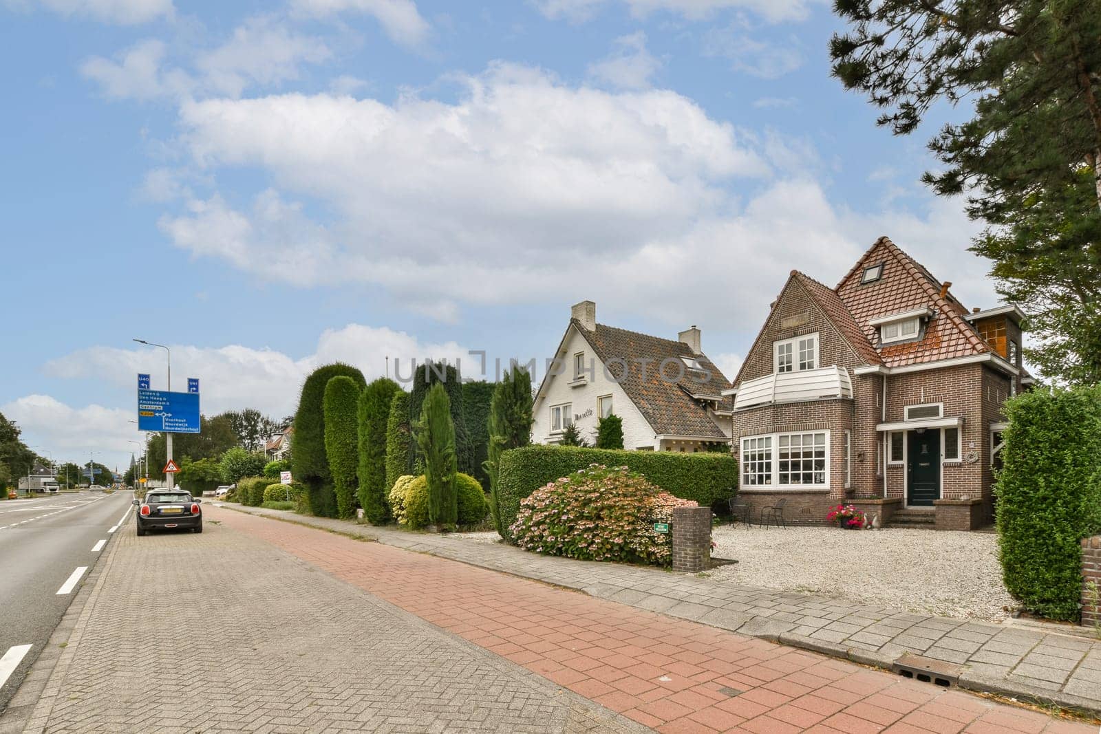 A serene roadside scene featuring charming houses surrounded by lush greenery and well-maintained hedges, providing a picturesque urban landscape.
