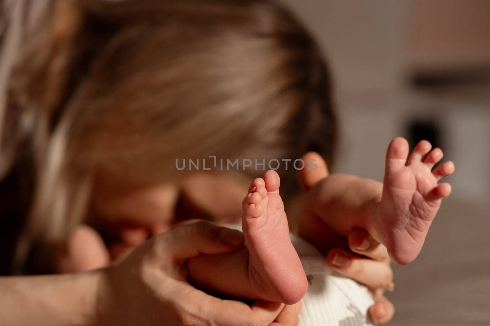 A mother gently holds her babys tiny feet while leaning in for a kiss at home. The warm atmosphere captures their close bond in a loving moment.