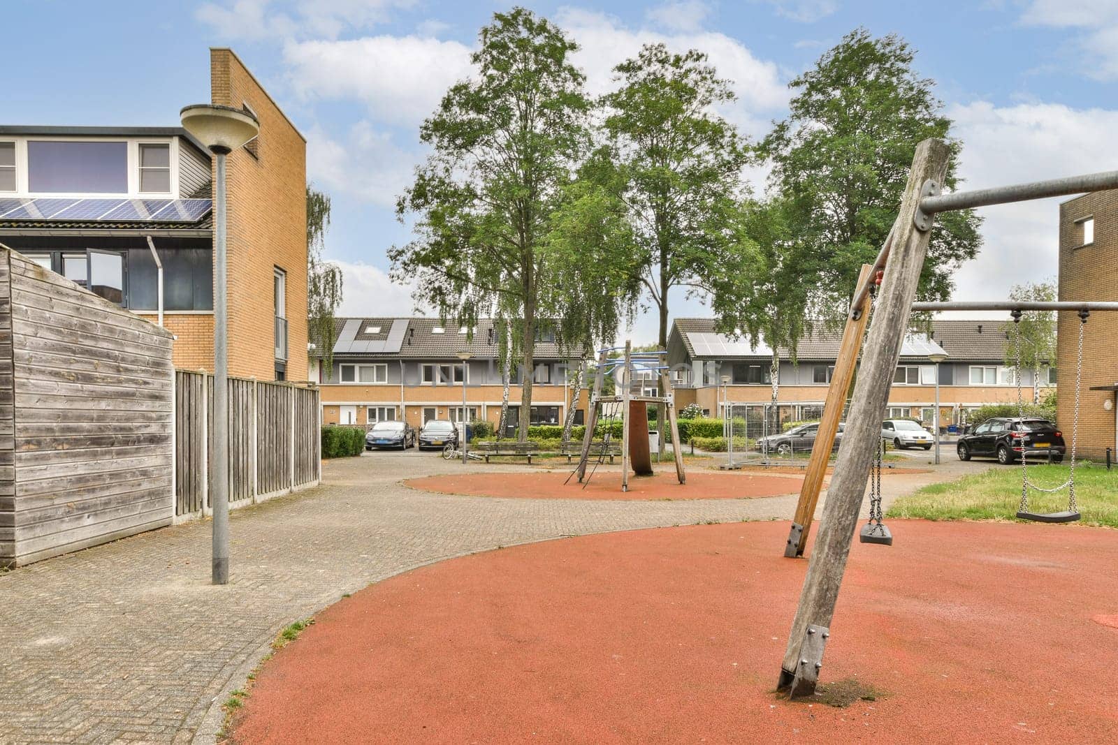 A well-designed playground featuring swings and playground equipment, set in a contemporary residential area with green trees and walkways.