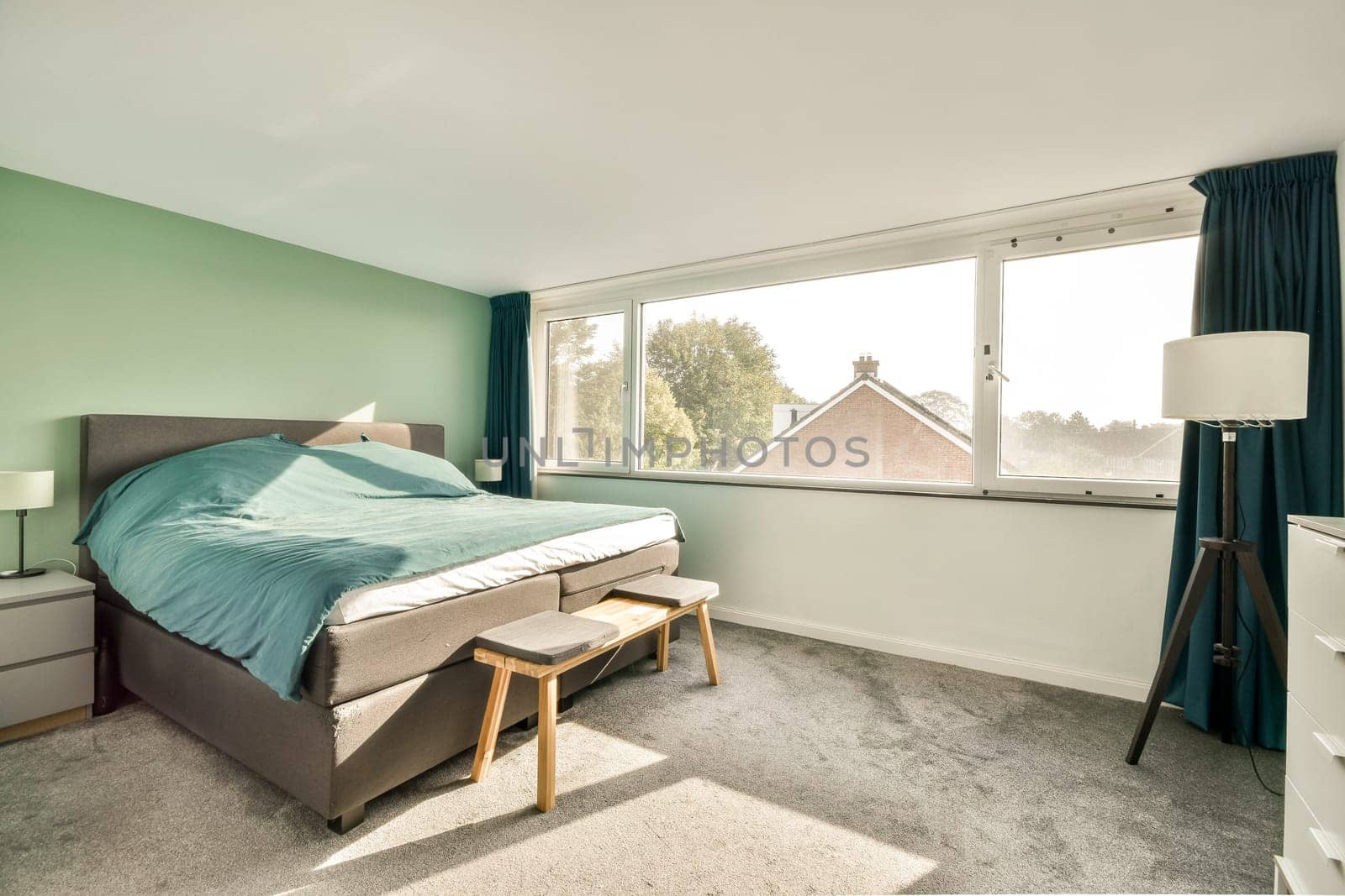 A serene and stylish bedroom showcasing a comfortable bed, soft textiles, and large windows inviting natural light, creating a calming atmosphere.