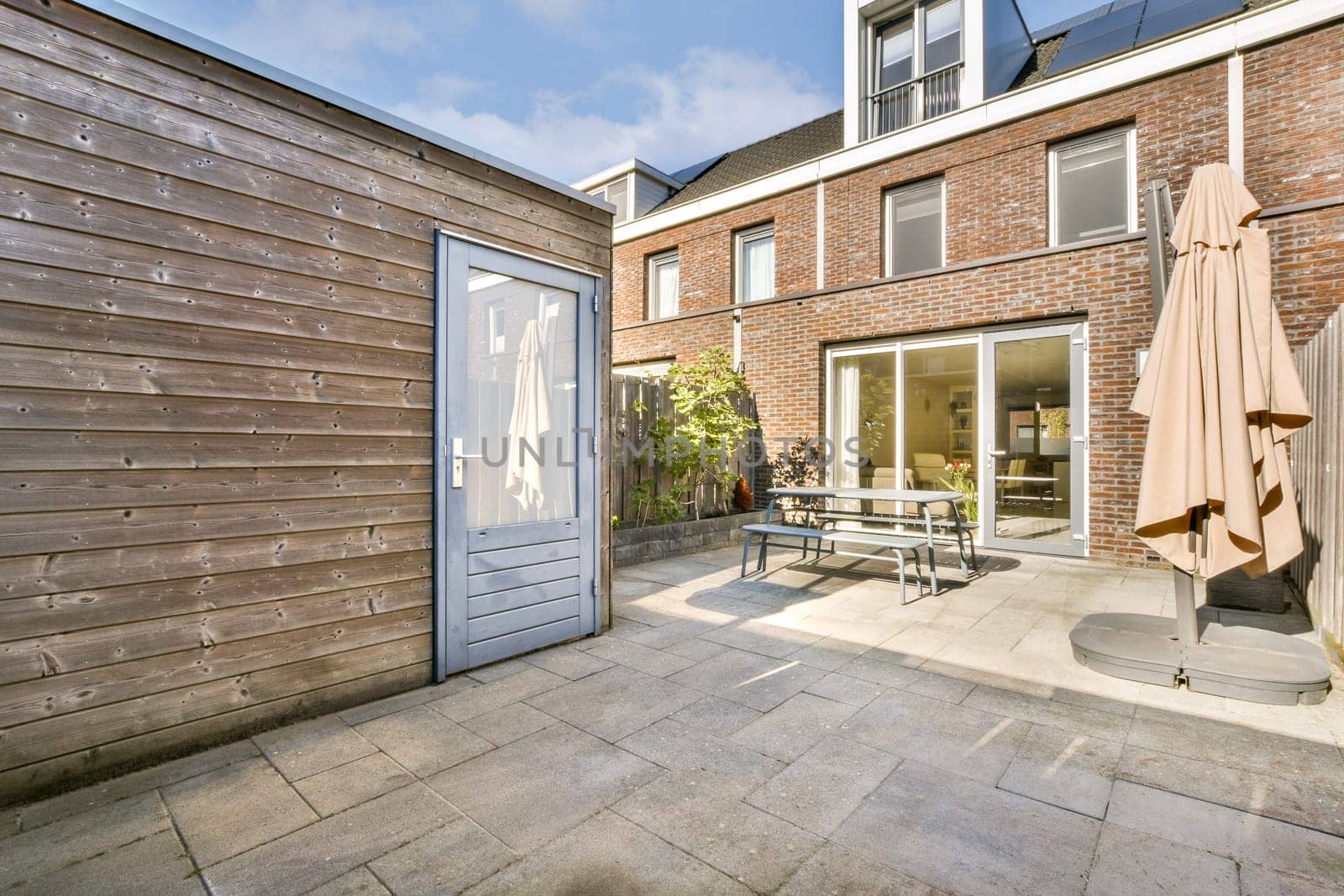A modern patio scene featuring a wooden wall, glass doors, and a stylish outdoor setup. The ambiance is bright and inviting, perfect for relaxation.