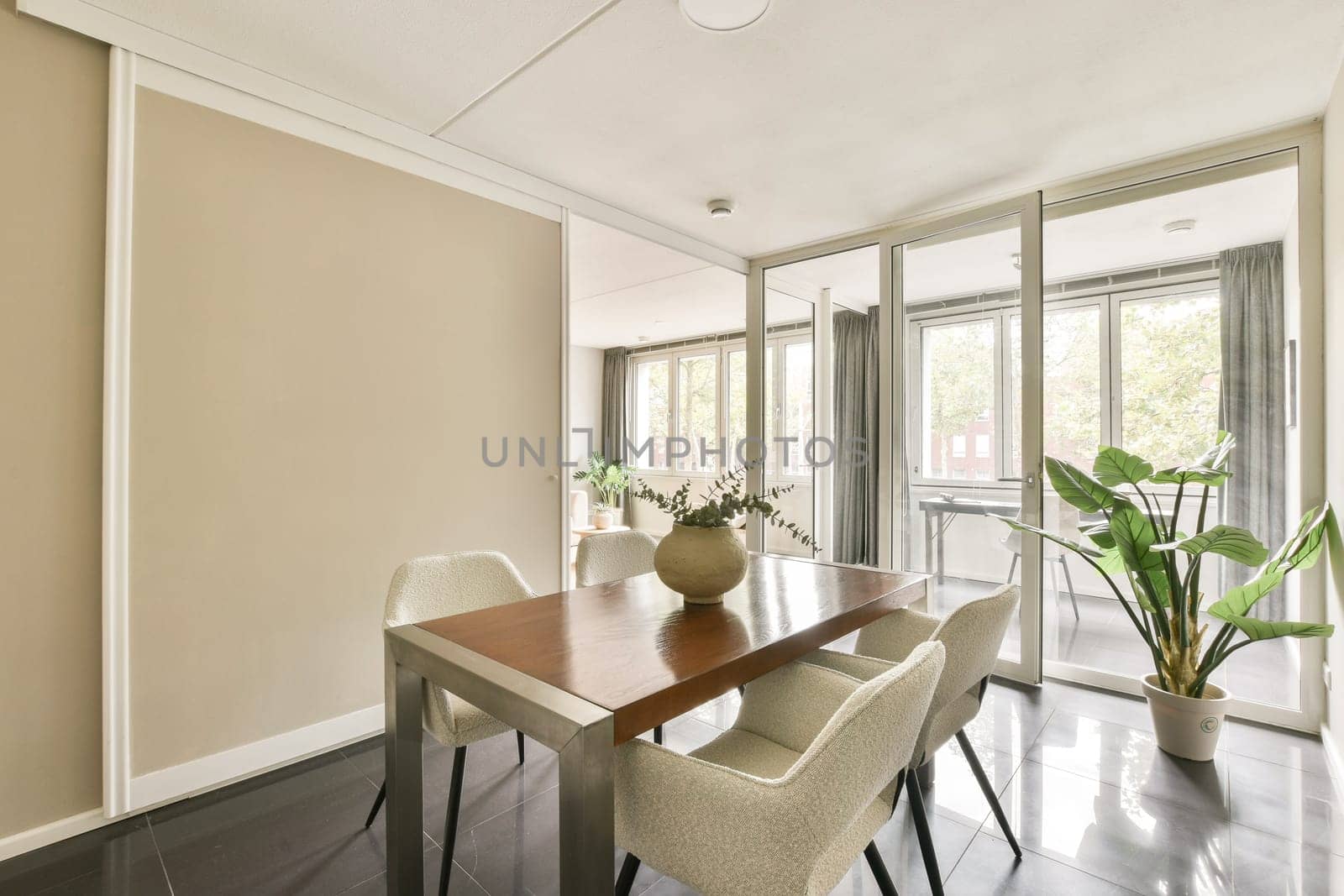 A stylish dining space featuring a wooden table, elegant chairs, and indoor plants, complemented by abundant natural light from large windows.