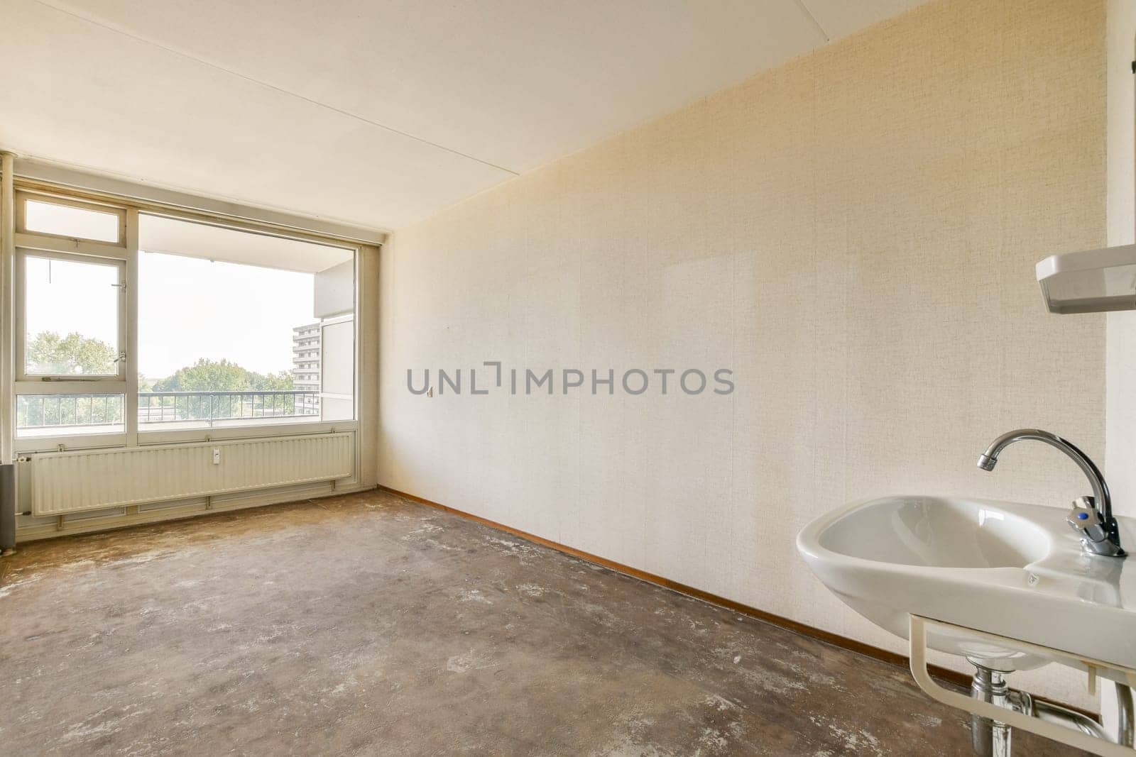 An empty room featuring large windows that allow natural light to flood in. The interior displays minimal decor and a simple design with basic amenities.
