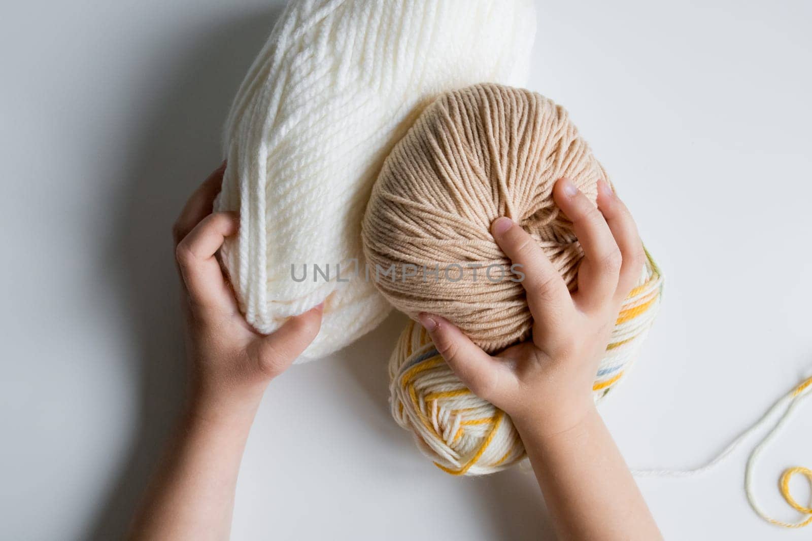 Child hands holding yarn balls. White, beige, and multicolored on white background.