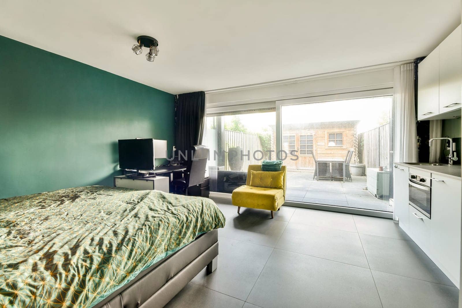 A contemporary interior featuring a bed, workspace, and large windows leading to an outdoor area, reflecting modern design aesthetics.