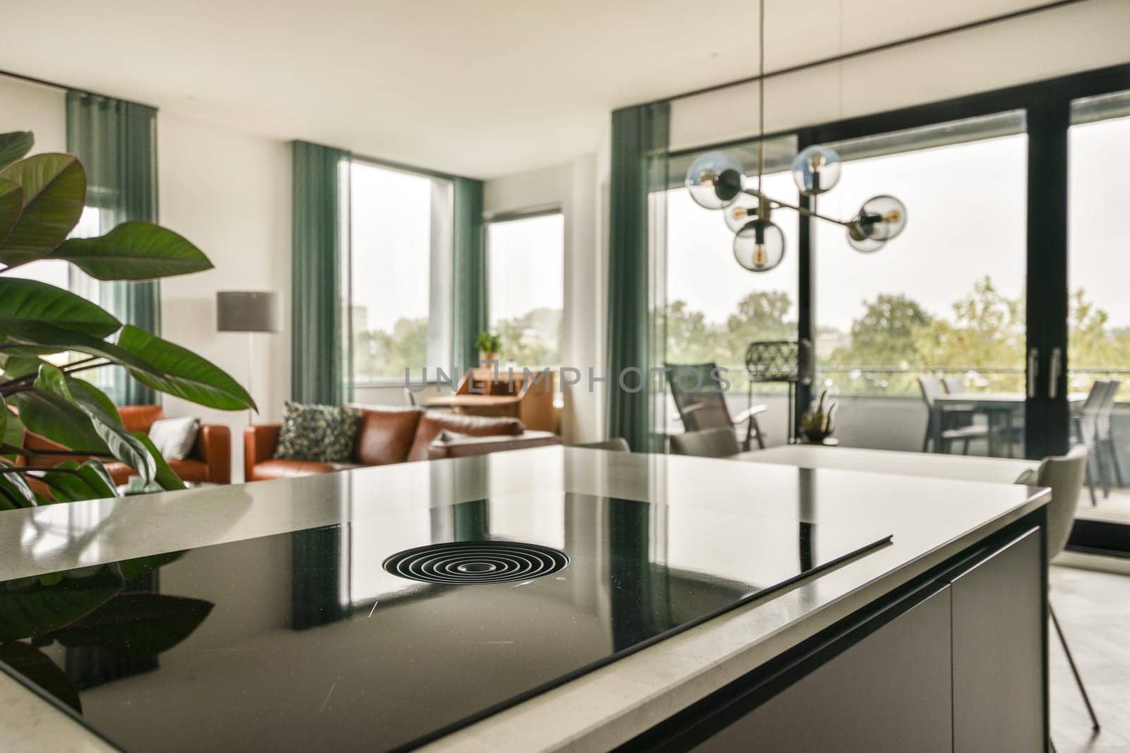 A stylish modern kitchen featuring sleek furnishings, large windows, and greenery, creating a bright, inviting atmosphere for cooking and entertaining.