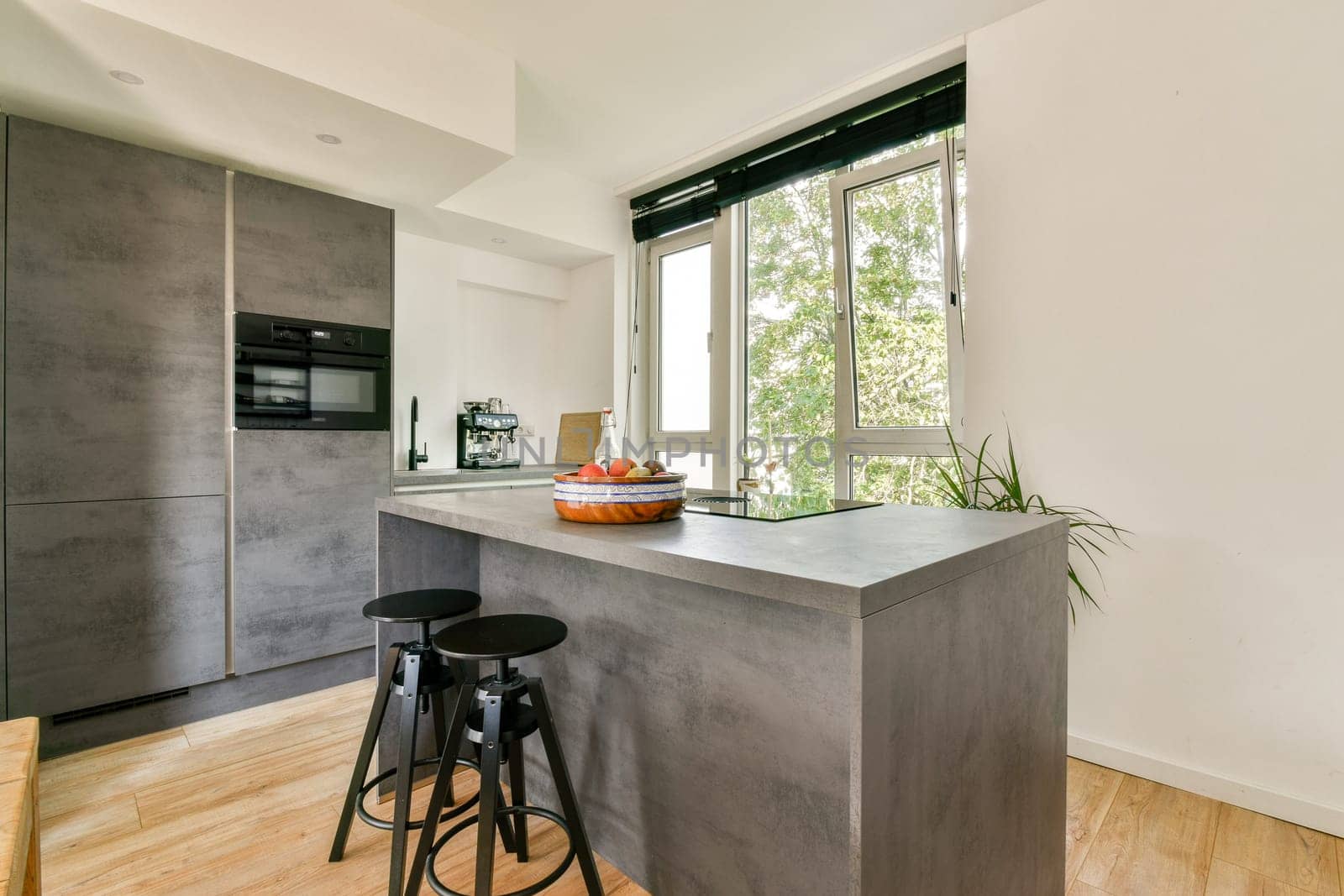 A sleek modern kitchen featuring a gray island with stools, natural light from large windows, and minimalist decor, creating an inviting cooking space.