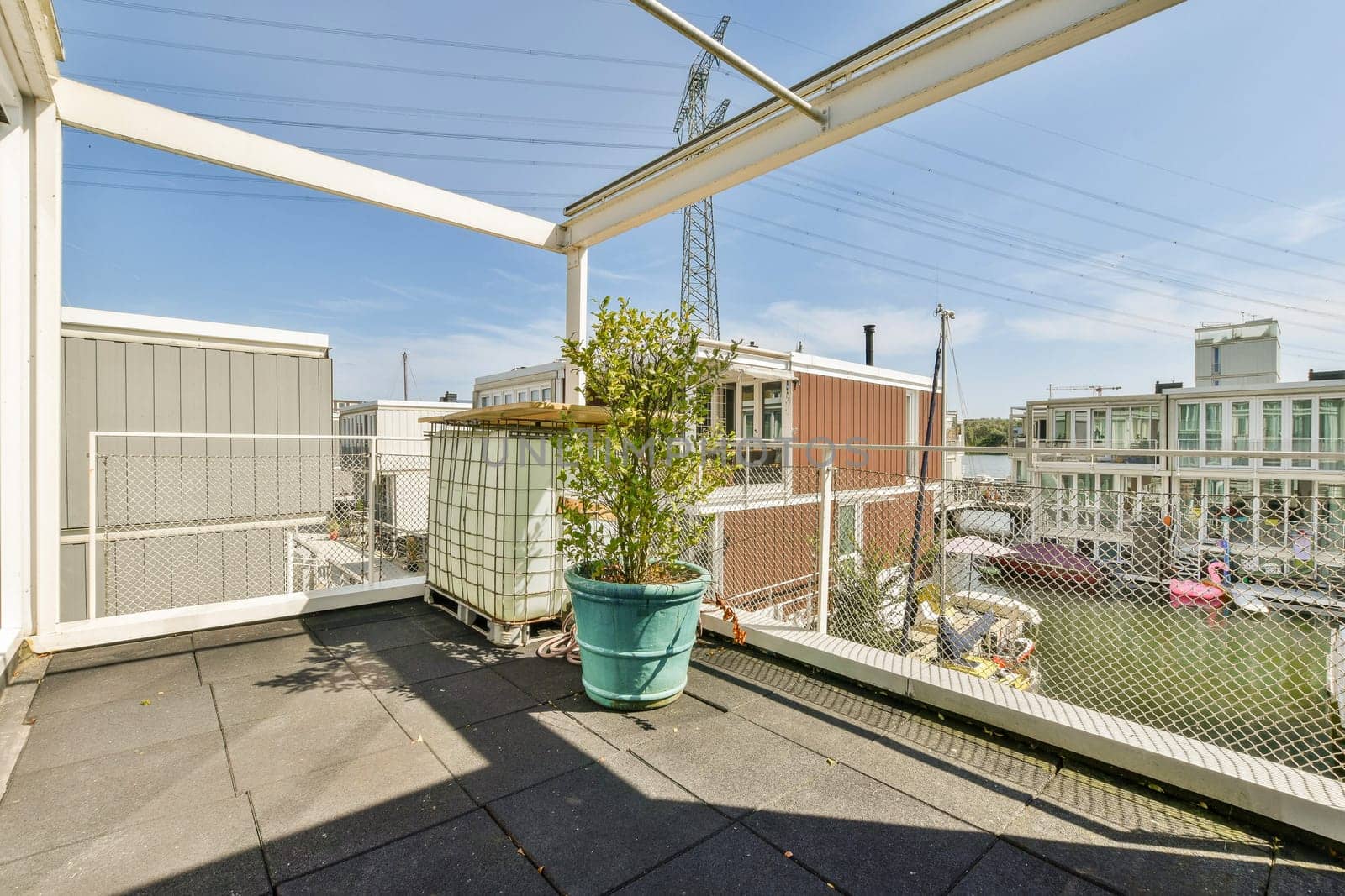 A stylish rooftop terrace featuring potted plants and a cityscape in the background. The scene captures urban living with a touch of greenery under a clear blue sky.