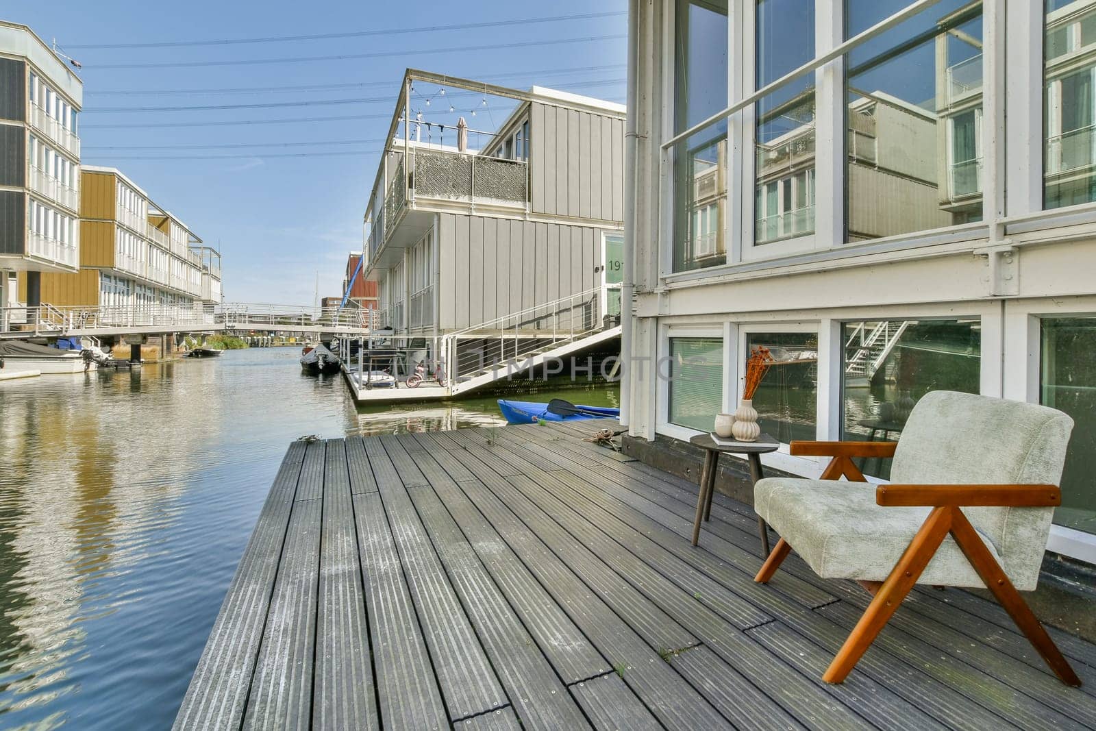 A stylish modern home with a wooden deck overlooking a calm canal, showcasing architectural elegance and serene water views.