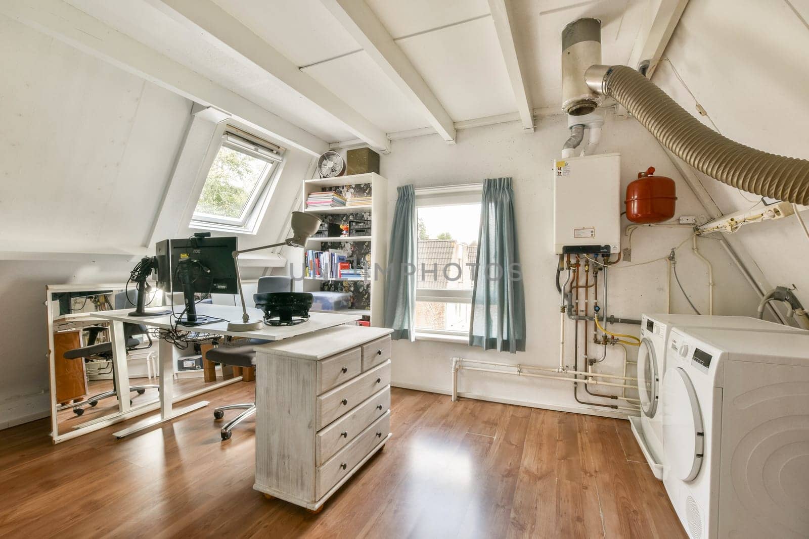 A well-organized home office featuring a desk, computer setup, and laundry area, illuminated by natural light through a large window.