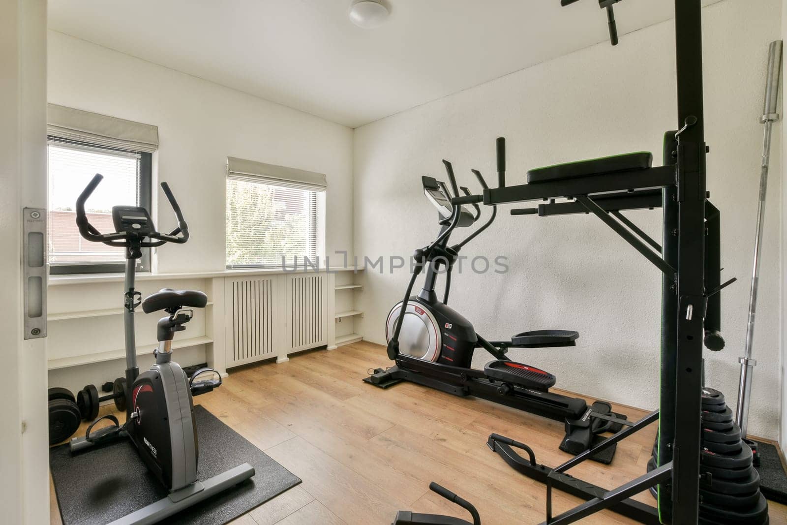 A well-lit home gym featuring exercise equipment such as an elliptical and stationary bike set against a minimalist backdrop.