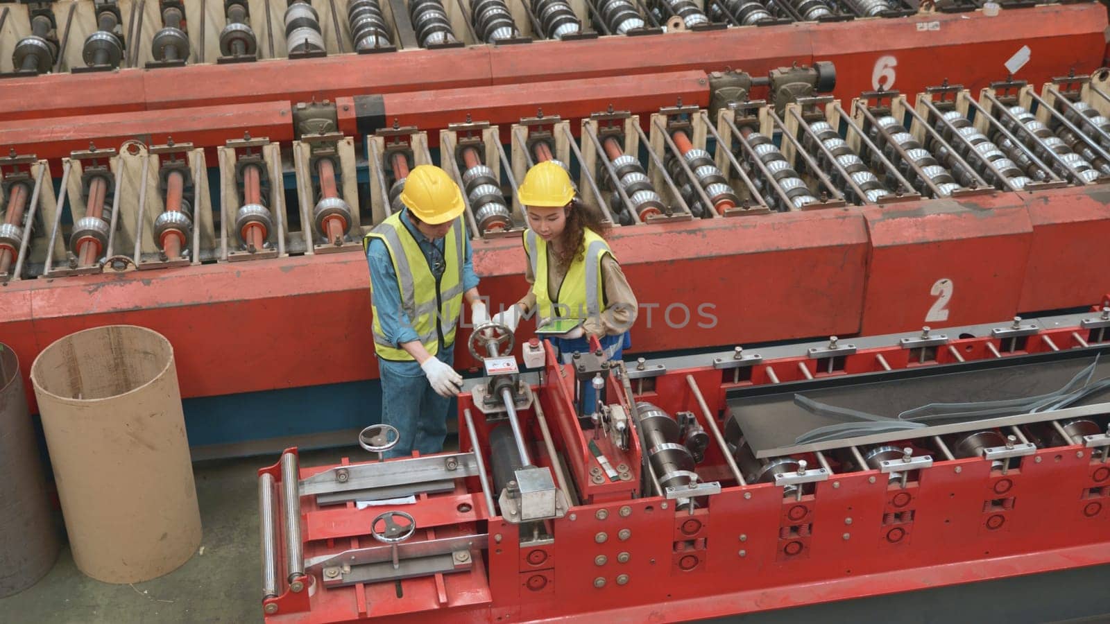 Engineer and operator wearing a safety suit maintaining machine in industrial metal sheet factory, team worker walk teaching help friend operate control heavy machine in factory with many equipment