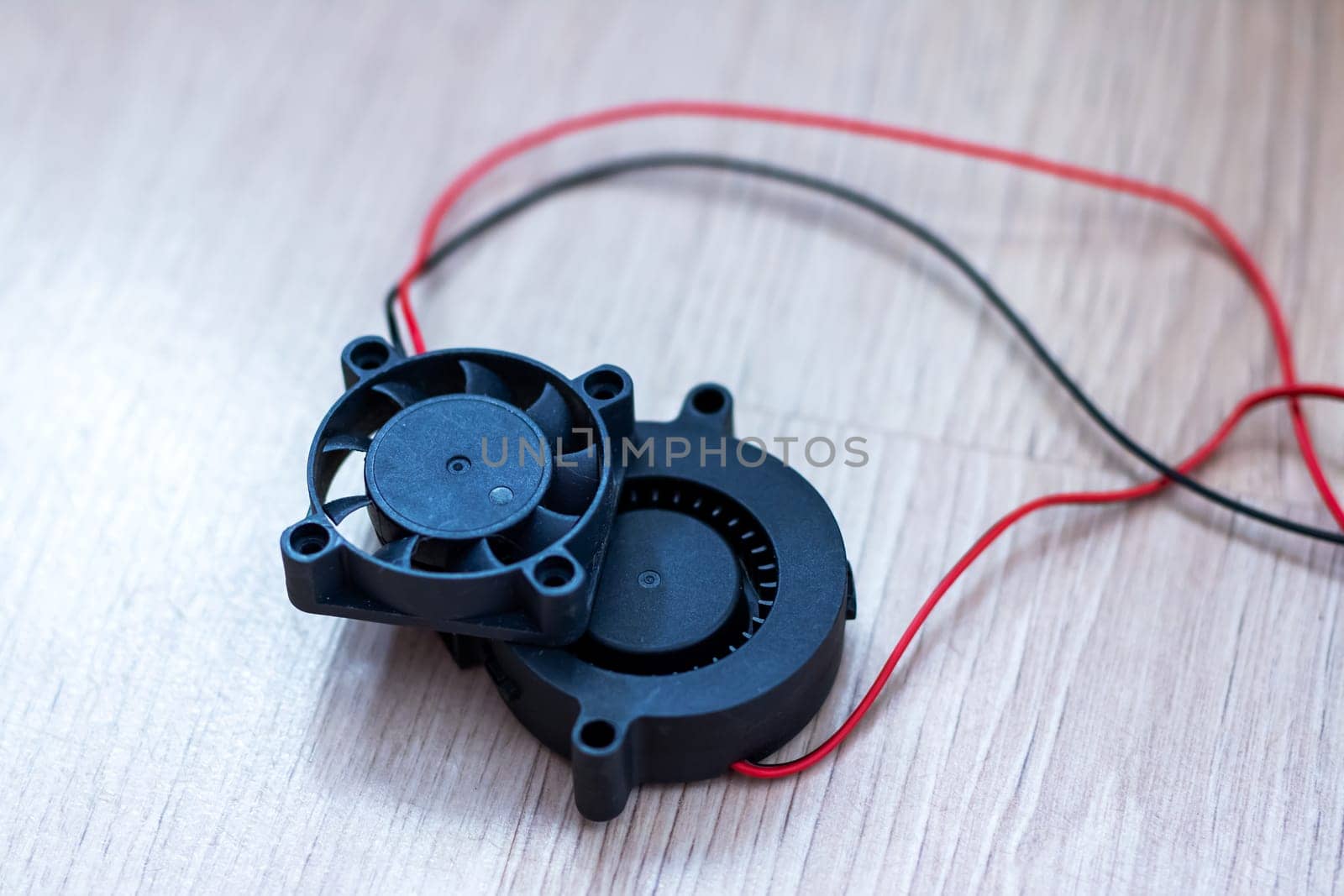 A compact, smallsized black fan that features red wires connected to it for its functioning and operation purposes
