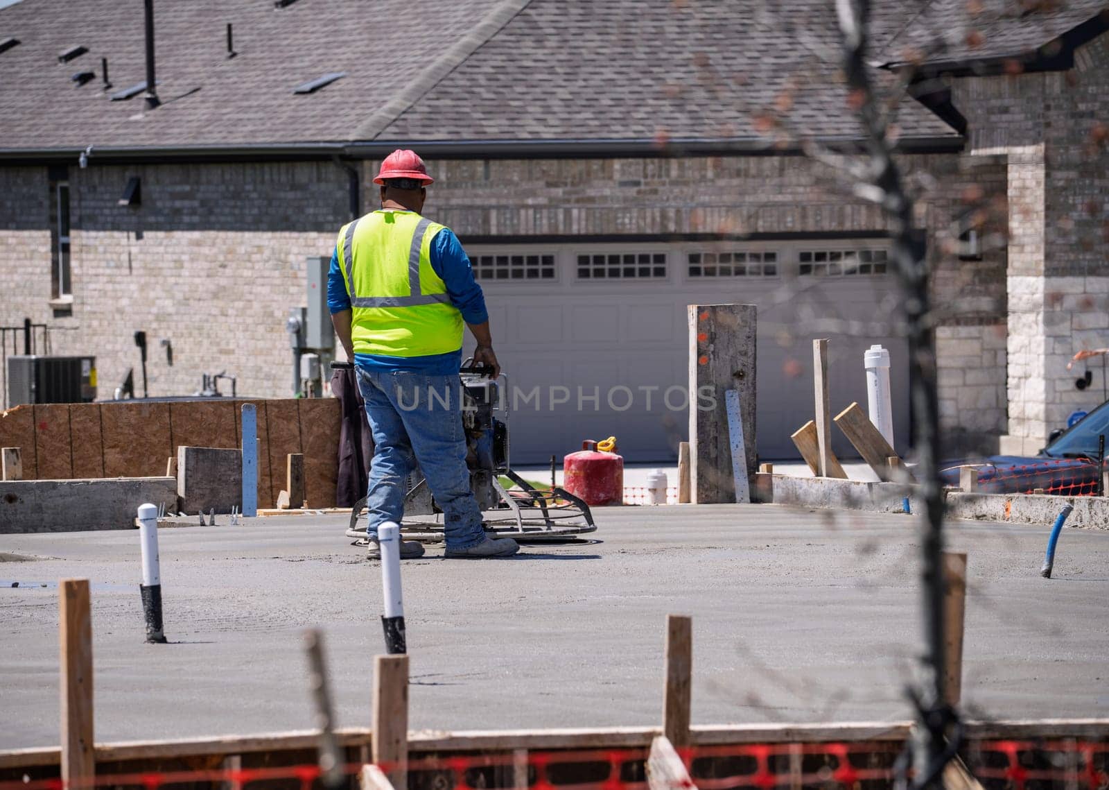 A construction worker uses a concrete finishing machine to smooth a fresh concrete slab on a new foundation
