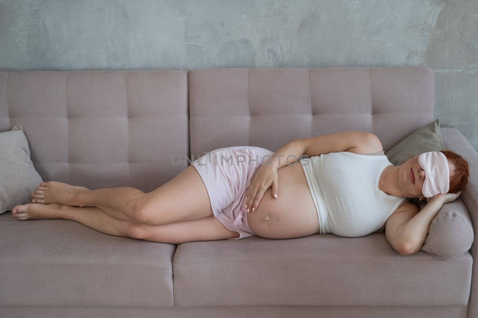 Caucasian pregnant woman sleeping on sofa wearing sleep mask